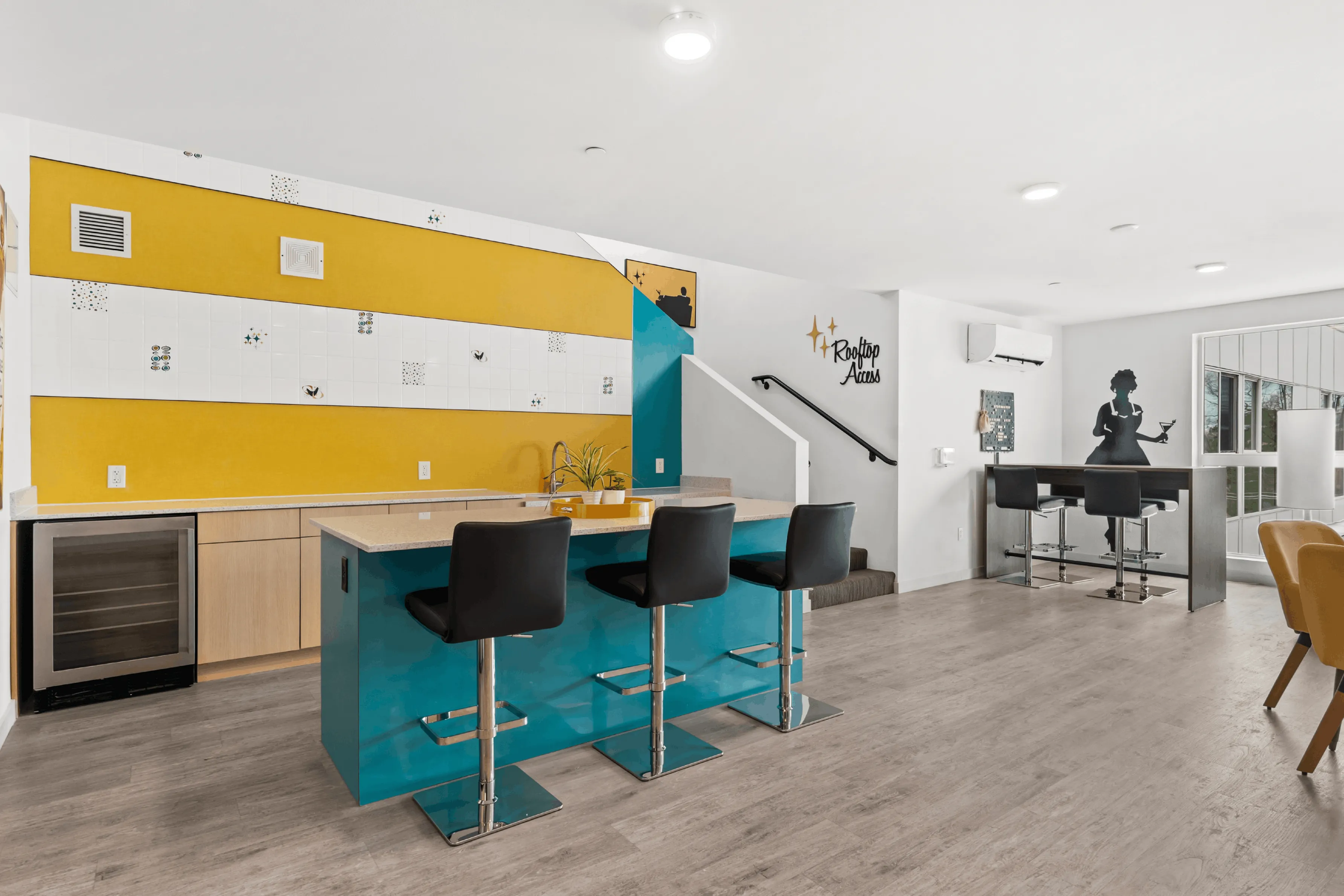 Vibrant modern kitchen with a bold yellow accent wall, stylish bar stools, and sleek countertops. Features a built-in wine cooler and artistic decor leading to rooftop access.