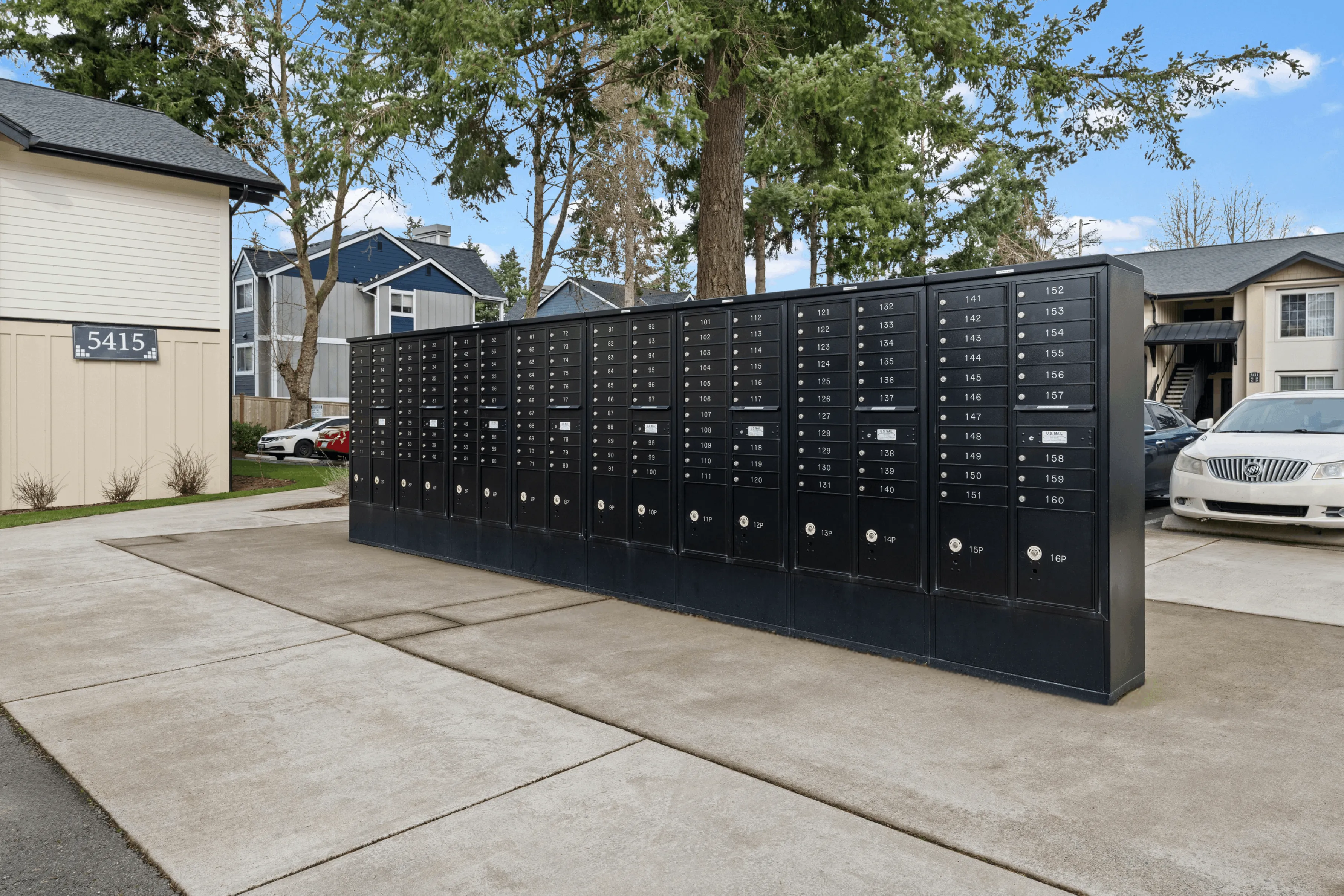 Charming apartment community showcasing modern mailboxes and lush green surroundings under a bright sky.