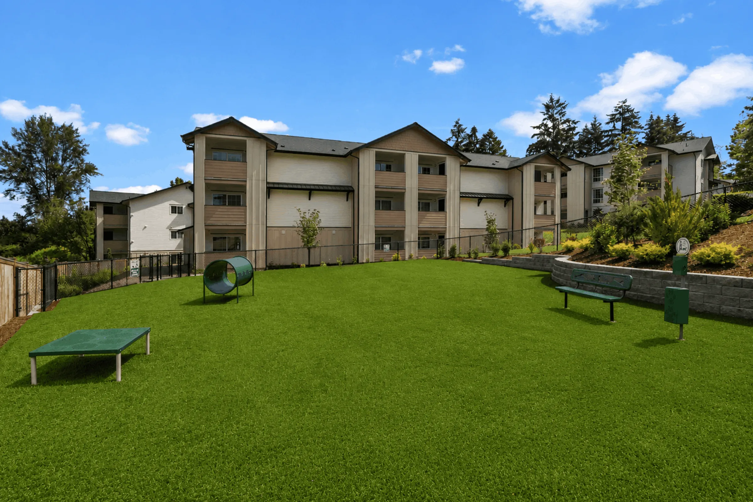 Charming apartment building with a spacious, lush green lawn featuring pet-friendly amenities and seating in a serene setting.