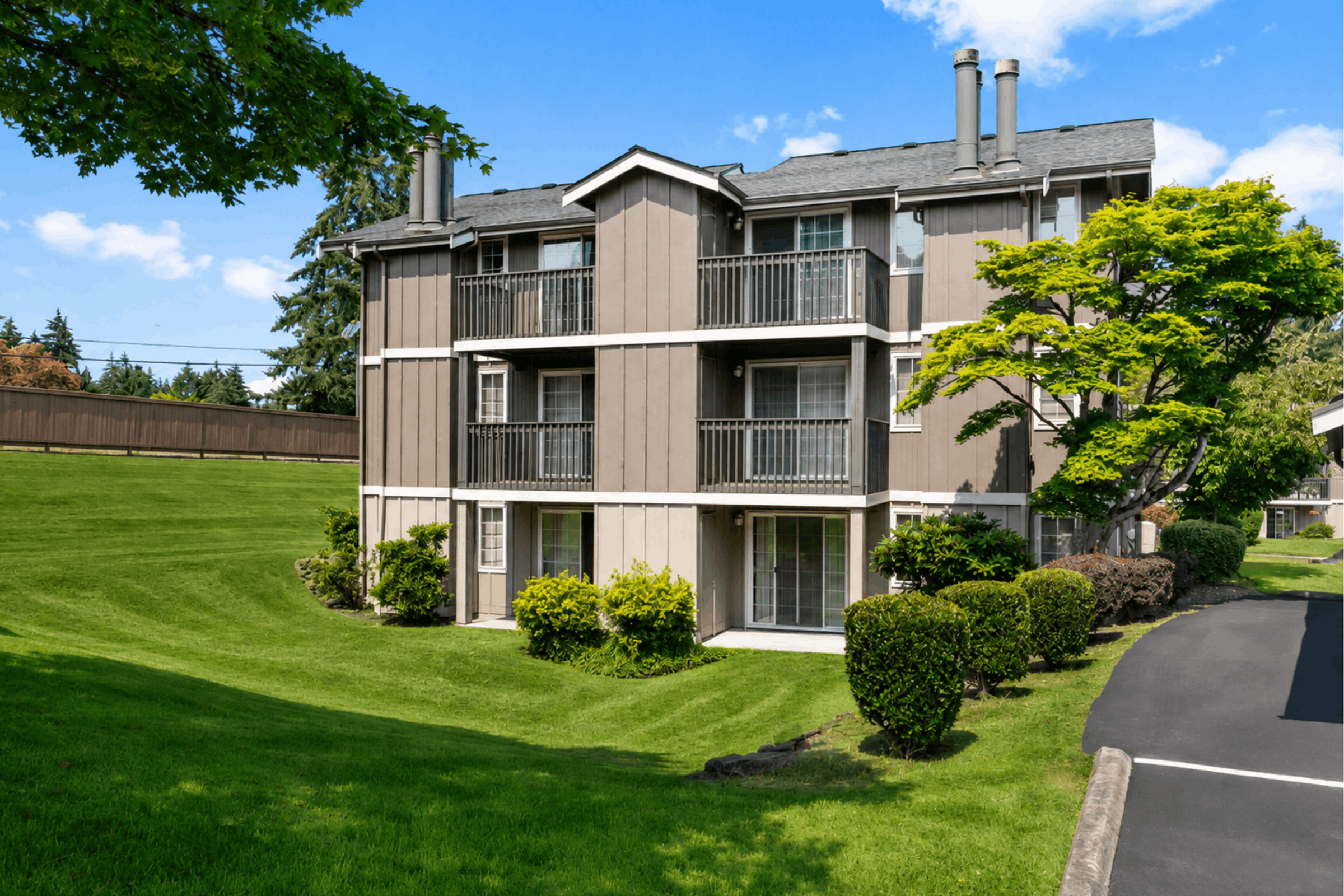 Charming three-story apartment building surrounded by lush green landscaping and vibrant trees under a bright blue sky.