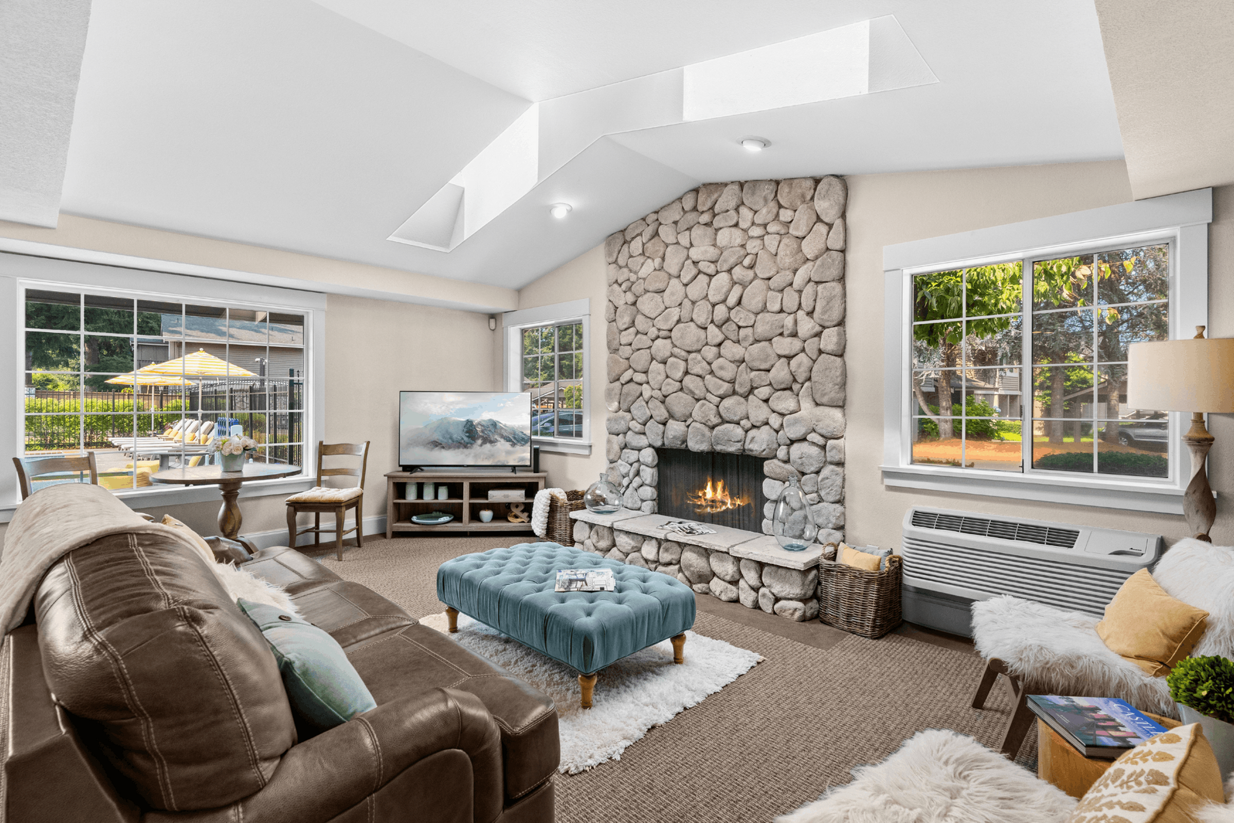 Inviting living room with a cozy stone fireplace, plush seating, and abundant natural light from large windows offering garden views.