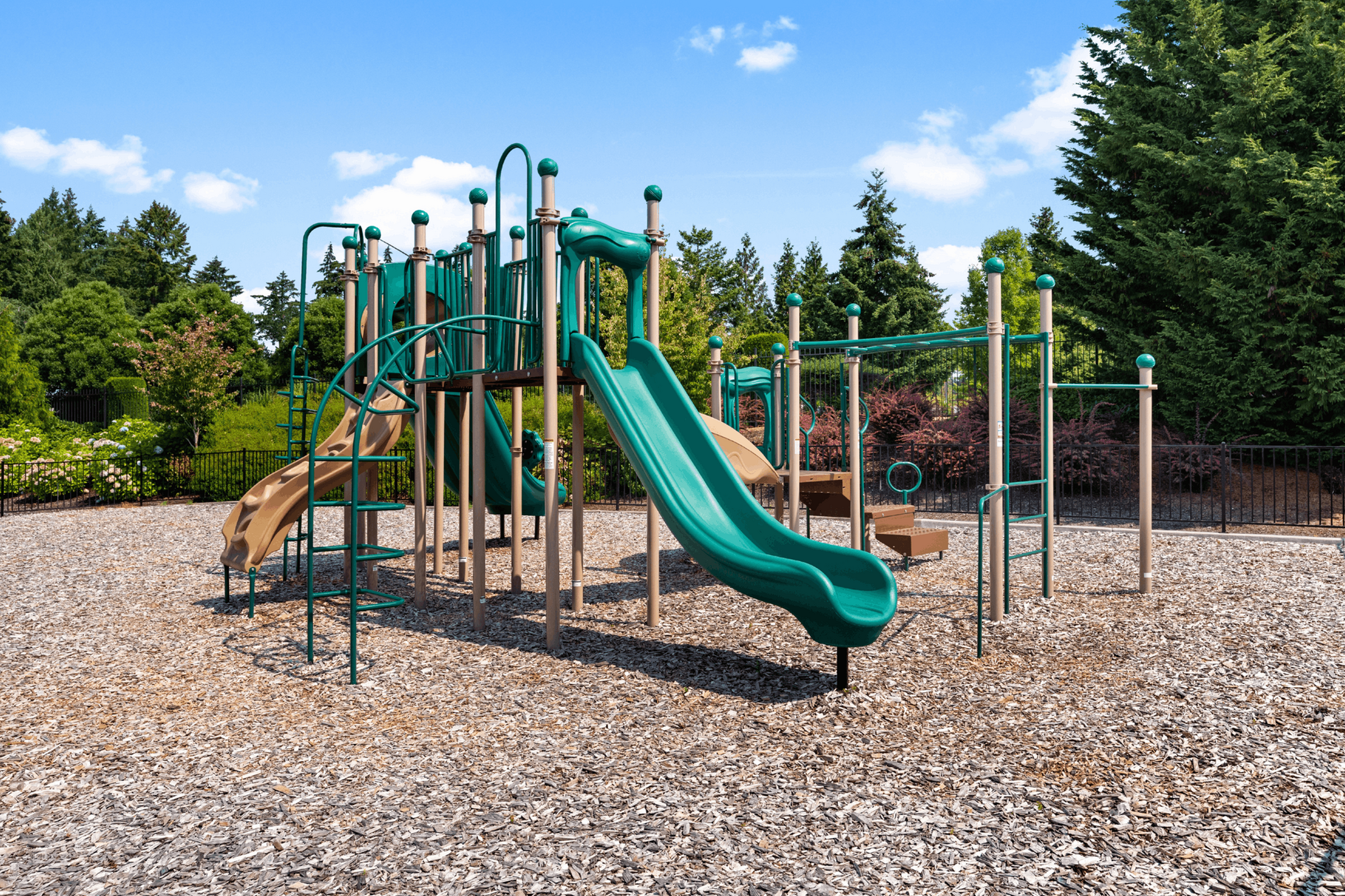 Vibrant playground featuring a green slide and climbing structure surrounded by lush greenery.