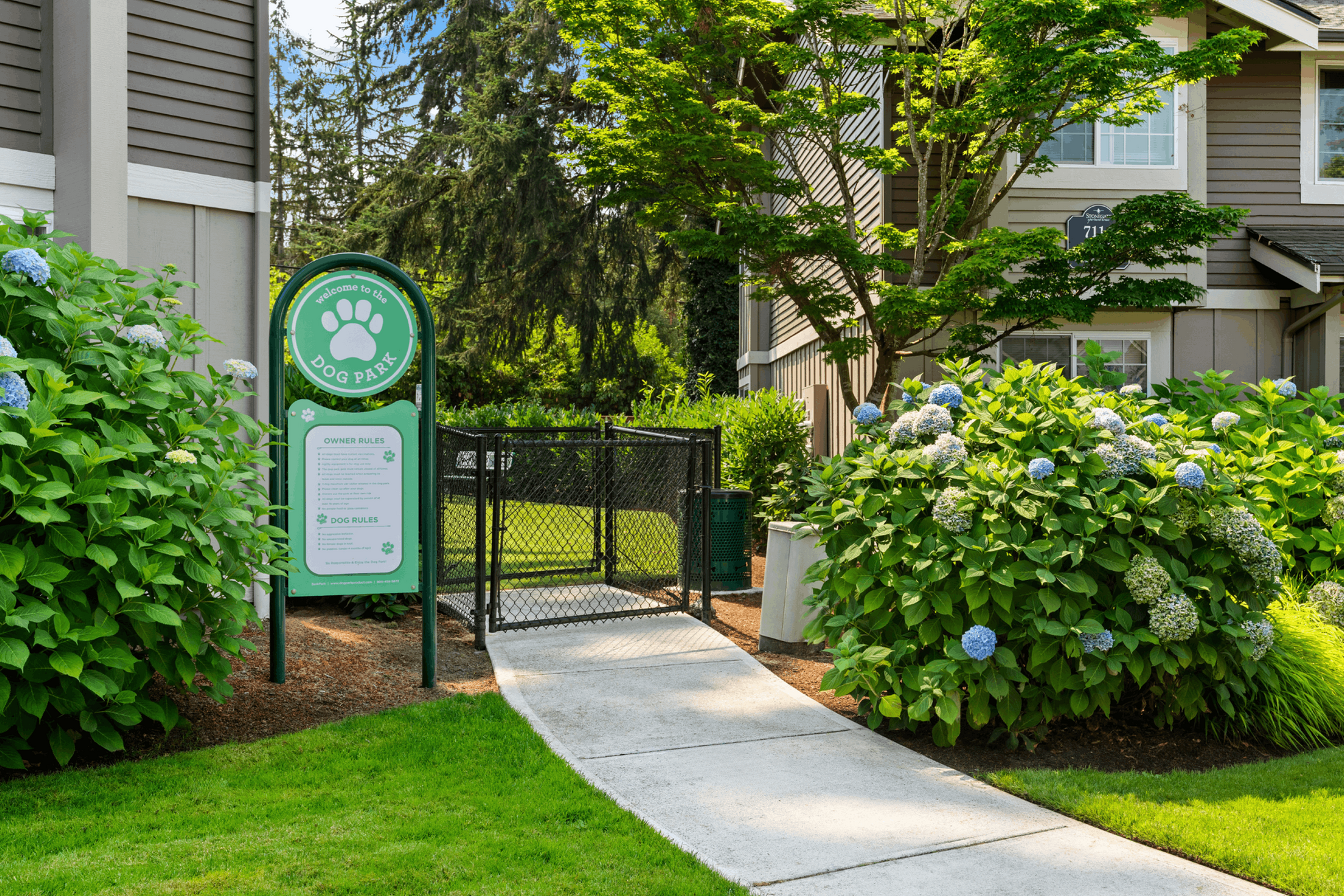 Charming dog park entrance with lush greenery and a welcoming pathway in a serene residential area.