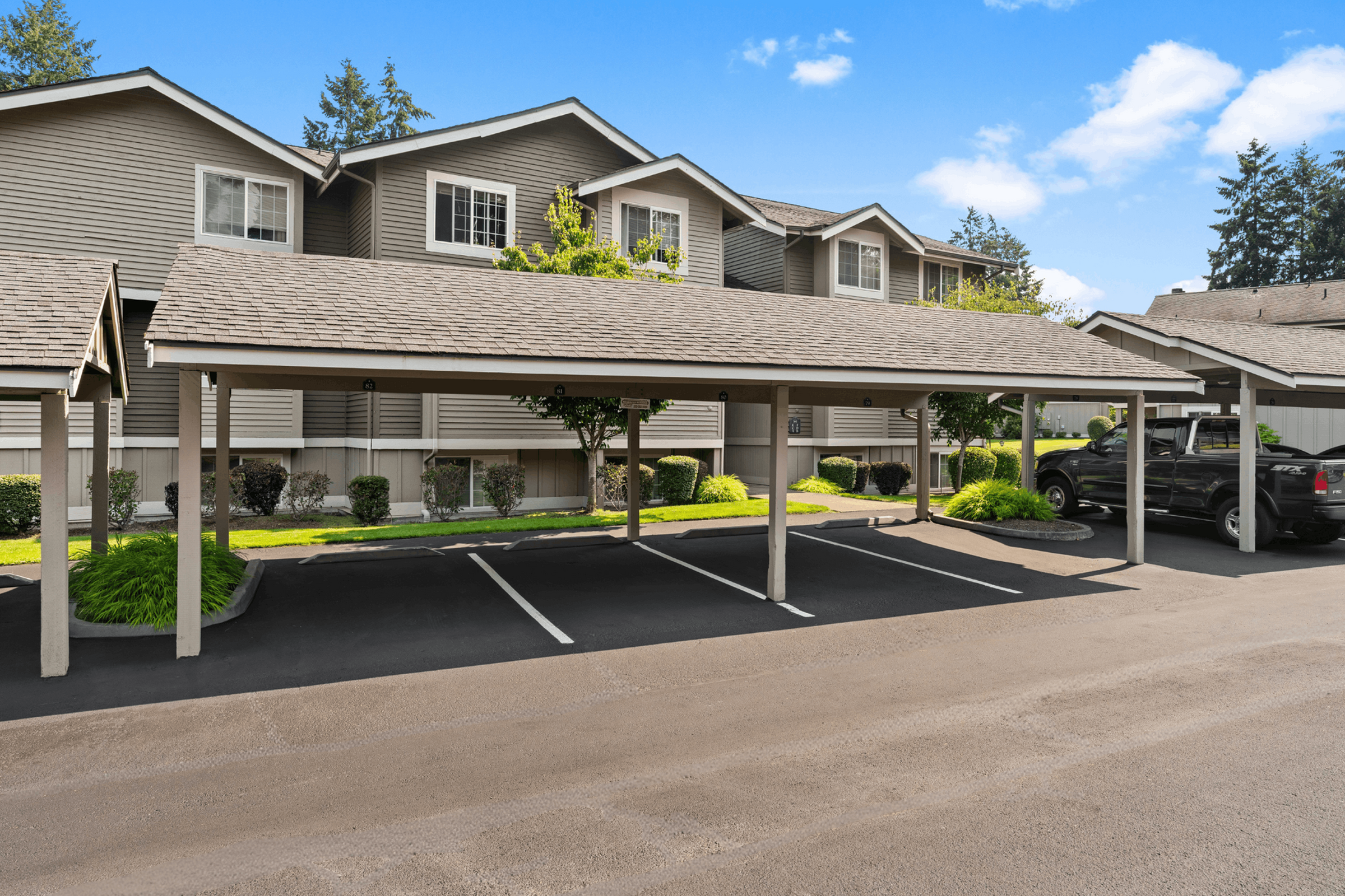 Charming apartment complex with covered parking, surrounded by lush greenery and clear blue skies.