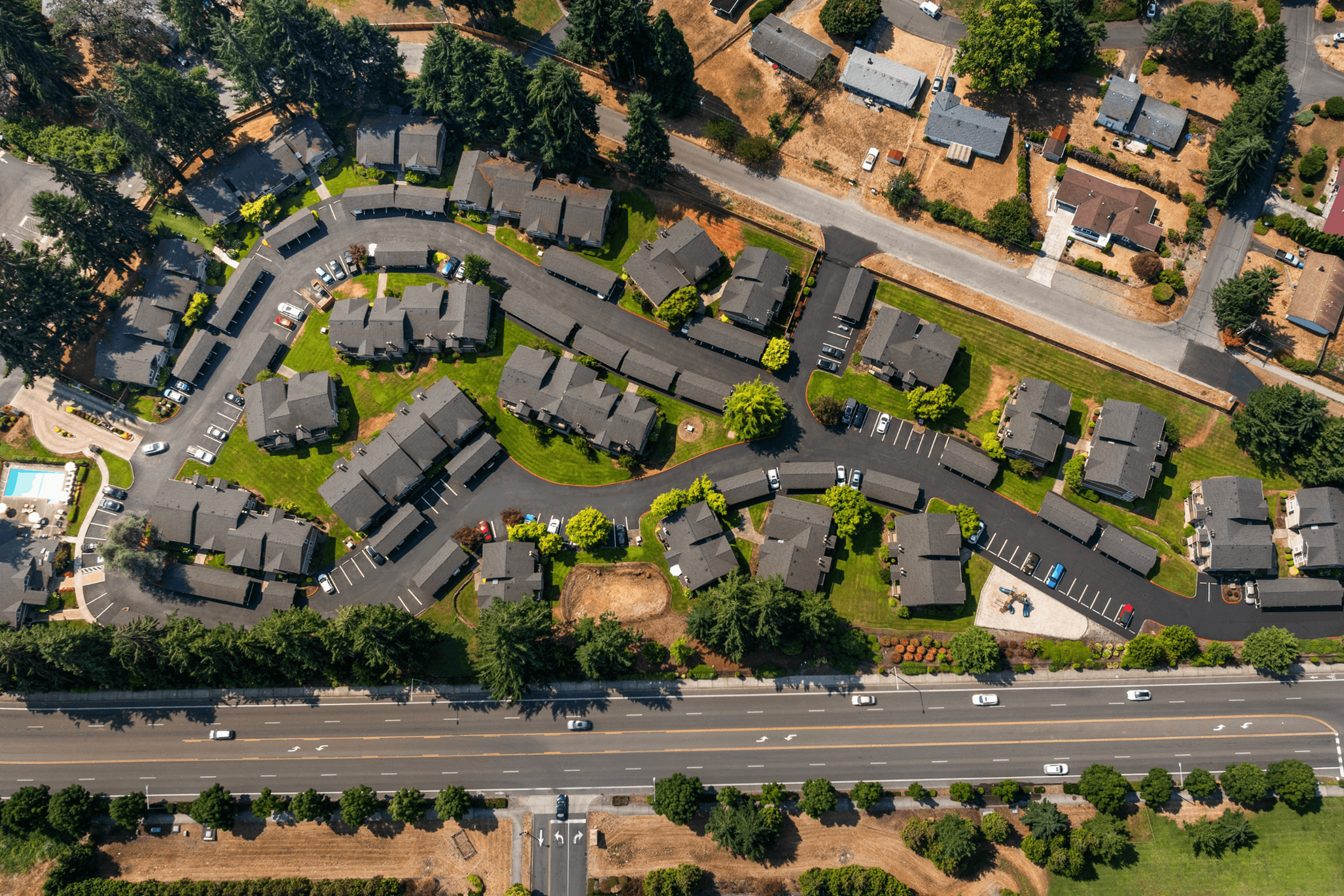 Aerial view of a charming residential community nestled among lush greenery, showcasing well-maintained homes with ample parking and nearby swimming pool.