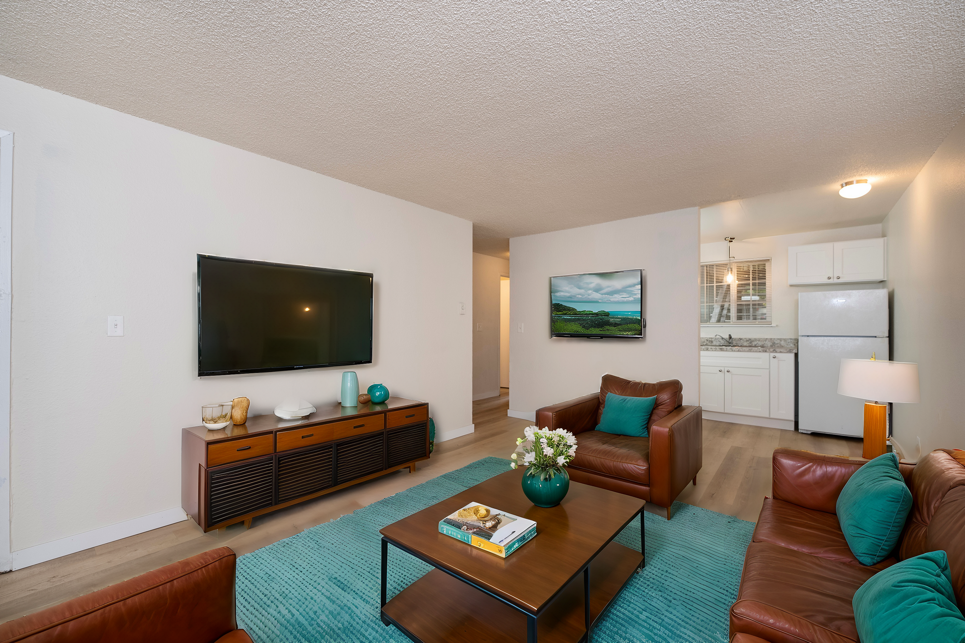 Inviting living room with stylish leather furniture, flat-screen TV, and a small kitchen in the background.