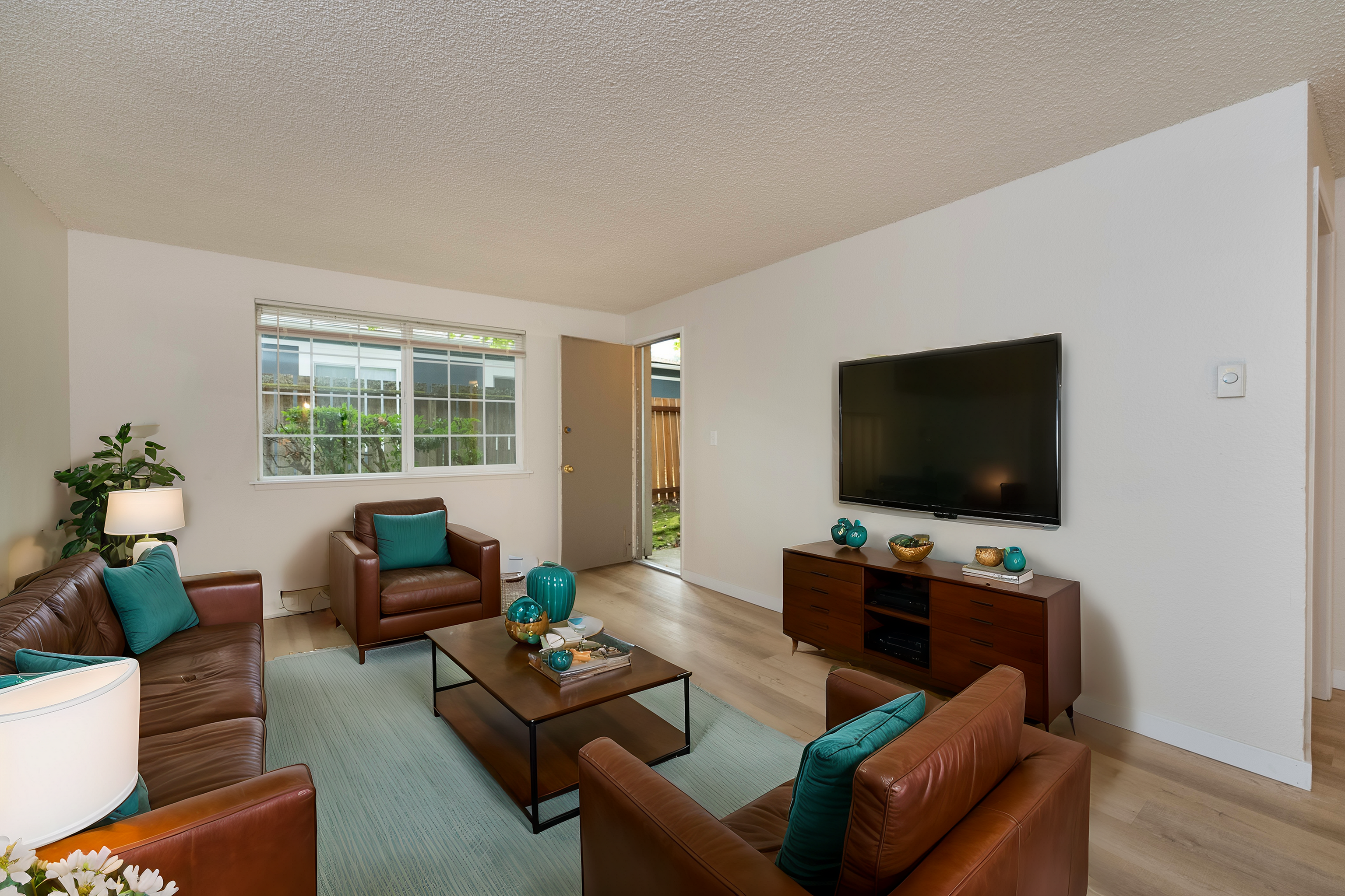 Inviting living room with brown leather sofas, teal accents, and a sleek TV setup.