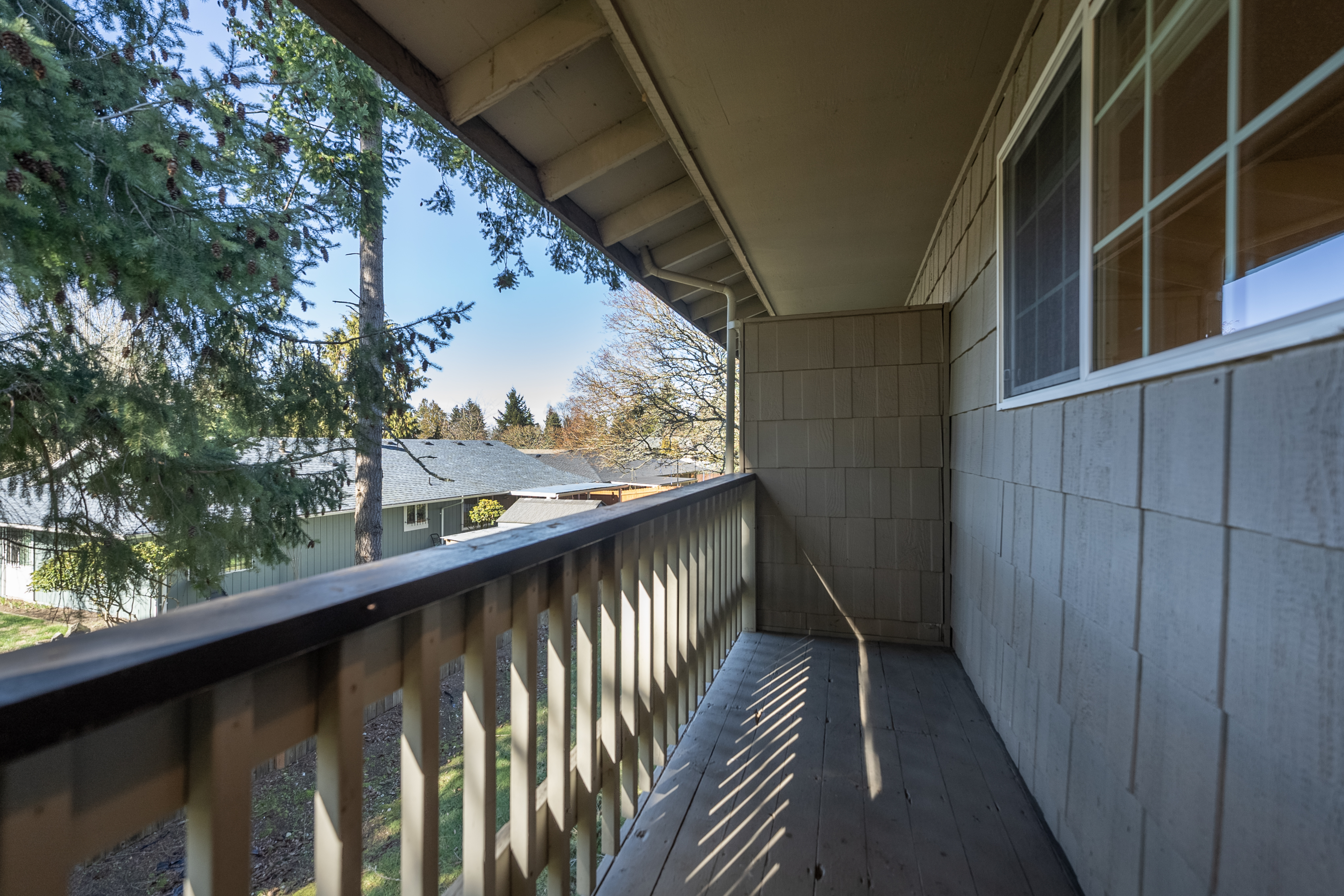 Charming wooden balcony overlooking a serene, tree-filled neighborhood.