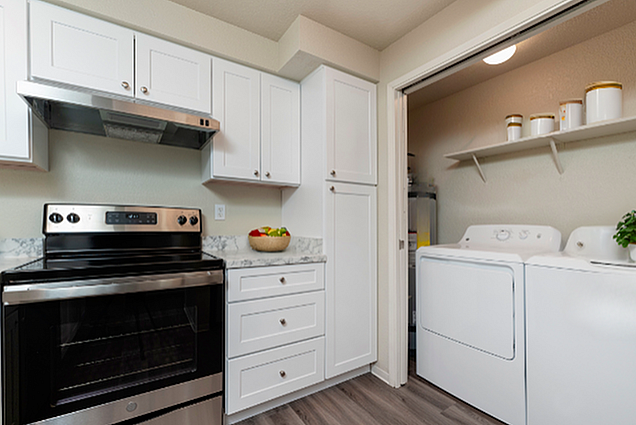 Bright kitchen with white cabinetry, sleek appliances, and adjacent laundry area with modern washer and dryer.