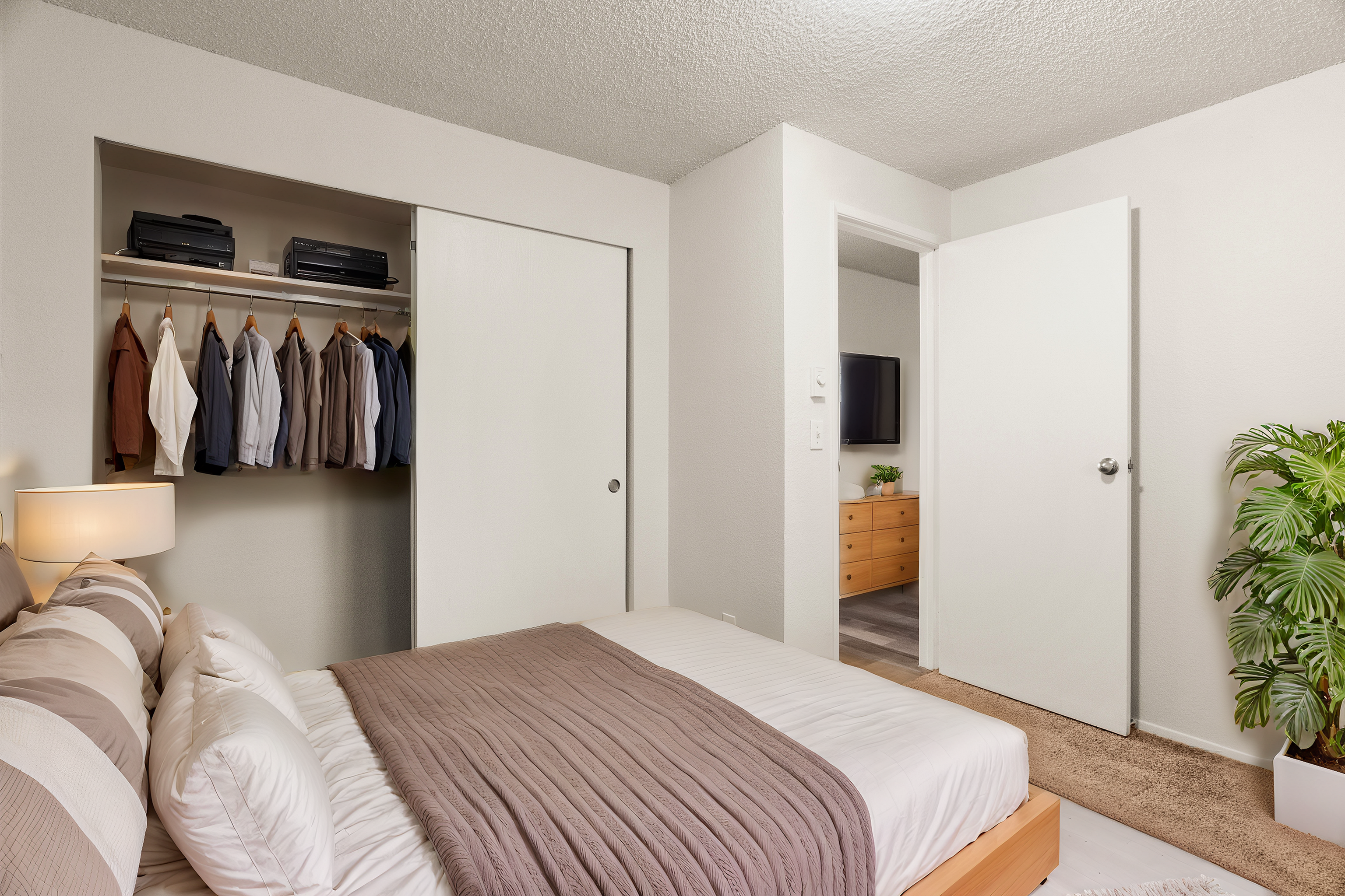 Modern bedroom with a neatly organized closet, soft bedding, and a touch of greenery.