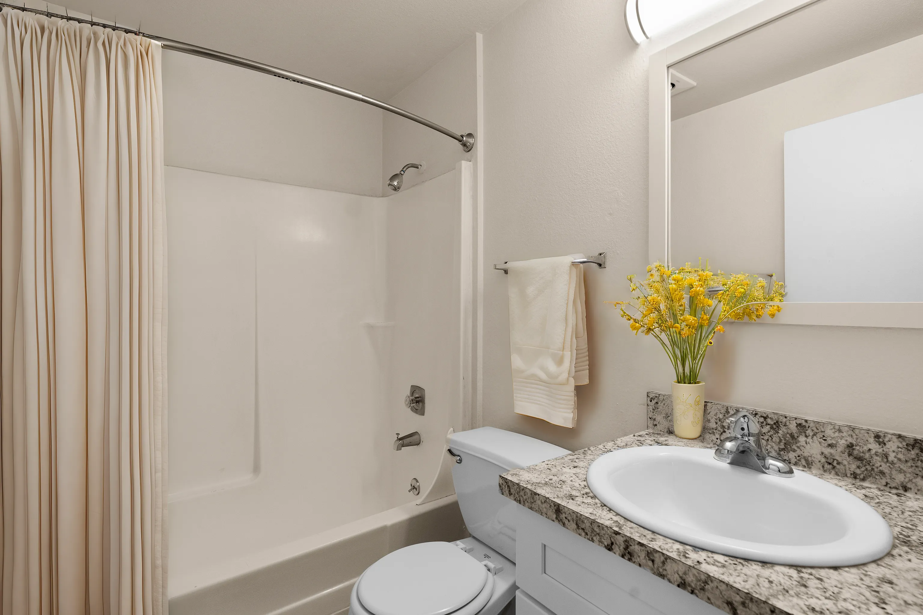 Elegant bathroom with a granite countertop, modern sink, fresh flowers, and a neatly arranged towel.