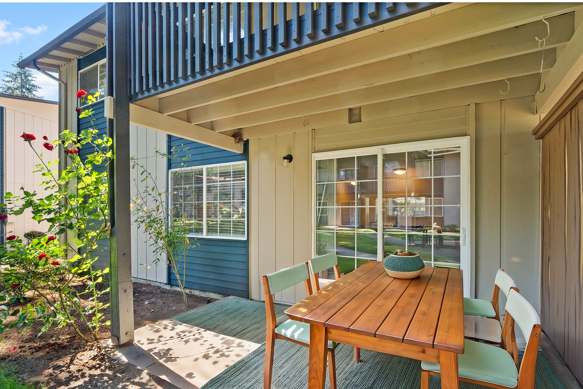 Cozy outdoor patio with wooden dining set and vibrant rose bushes.