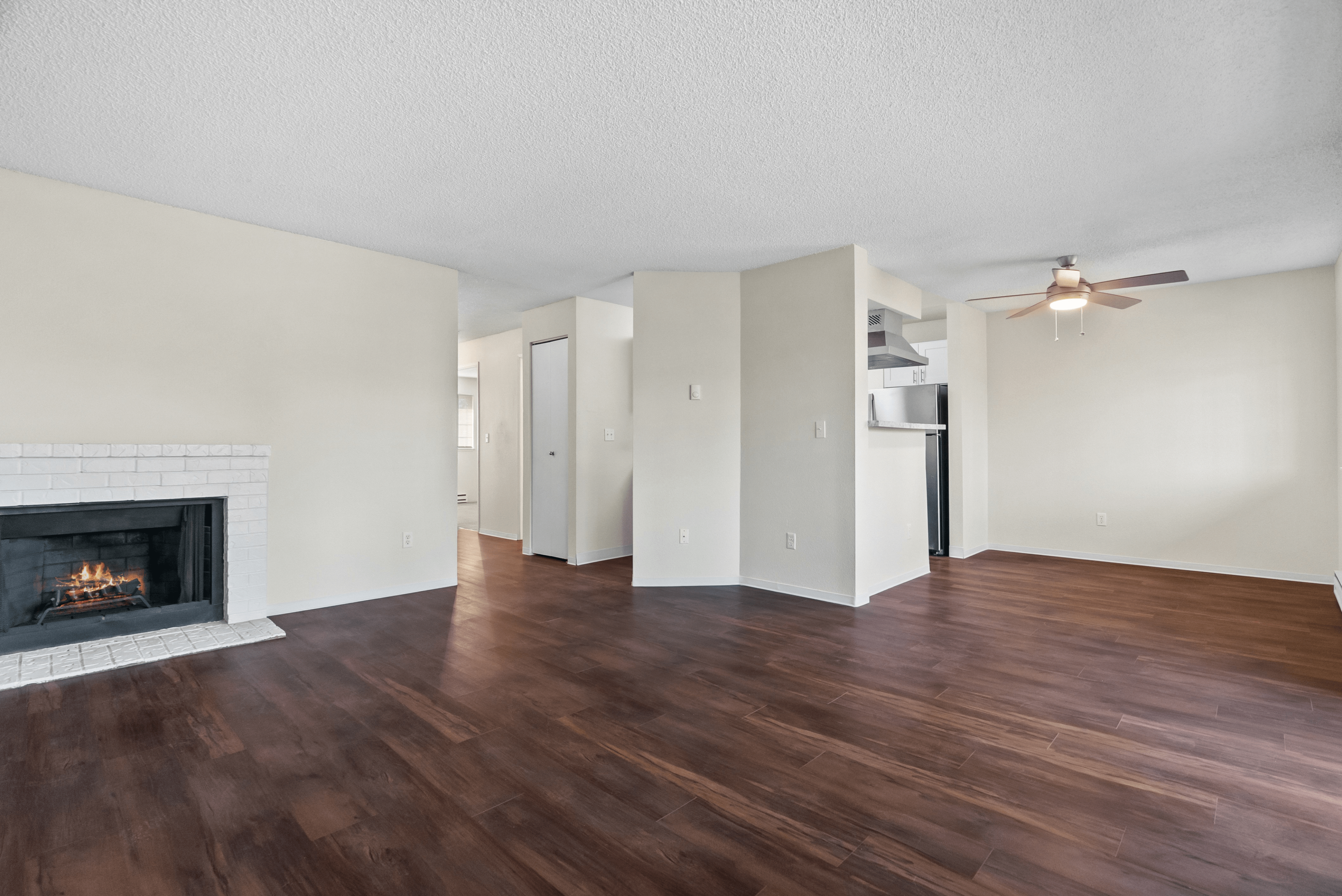 Bright open living area with hardwood floors, a cozy fireplace, and a ceiling fan.