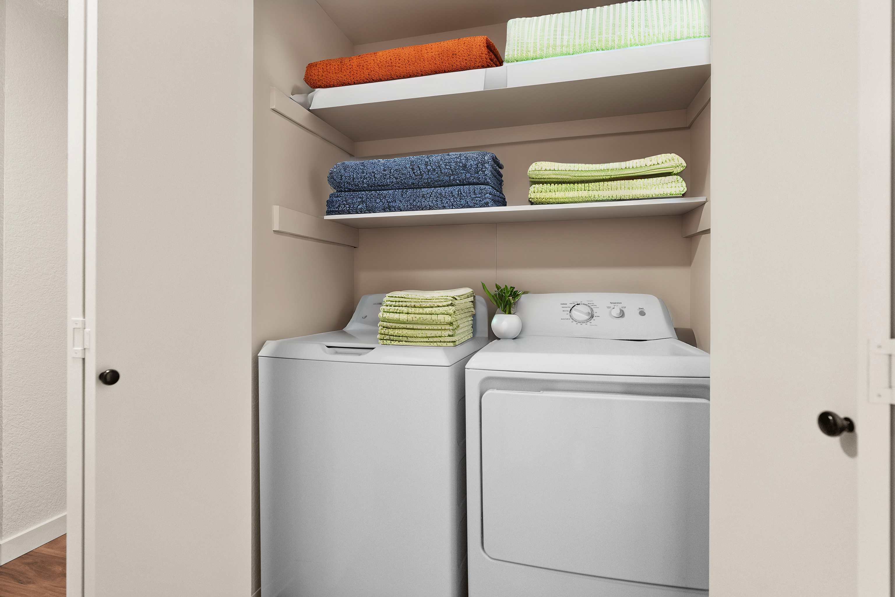 Compact laundry area with washer, dryer, and organized shelves with colorful towels.
