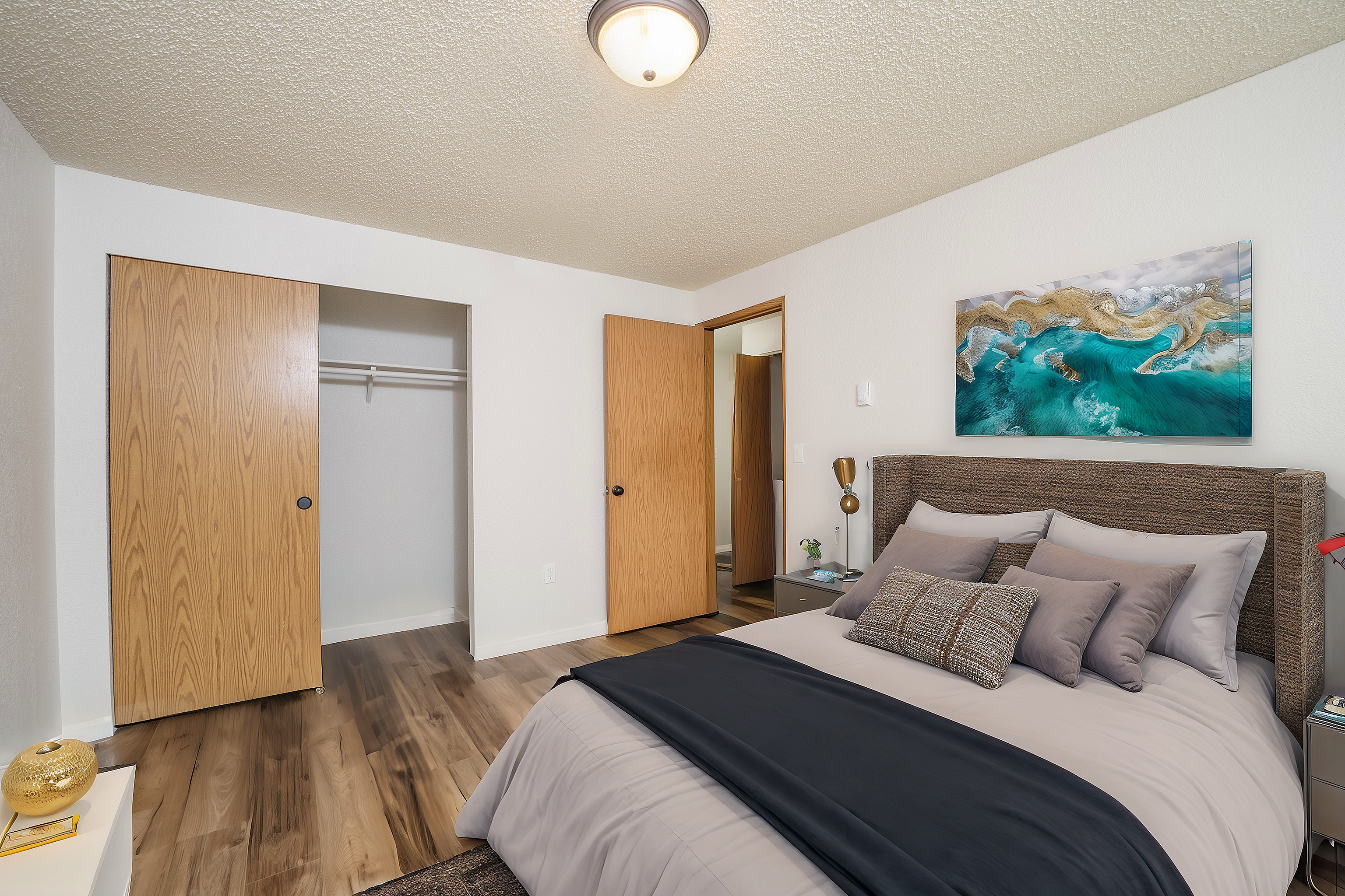Charming bedroom with wooden flooring, spacious closet, and stylish artwork above the bed.