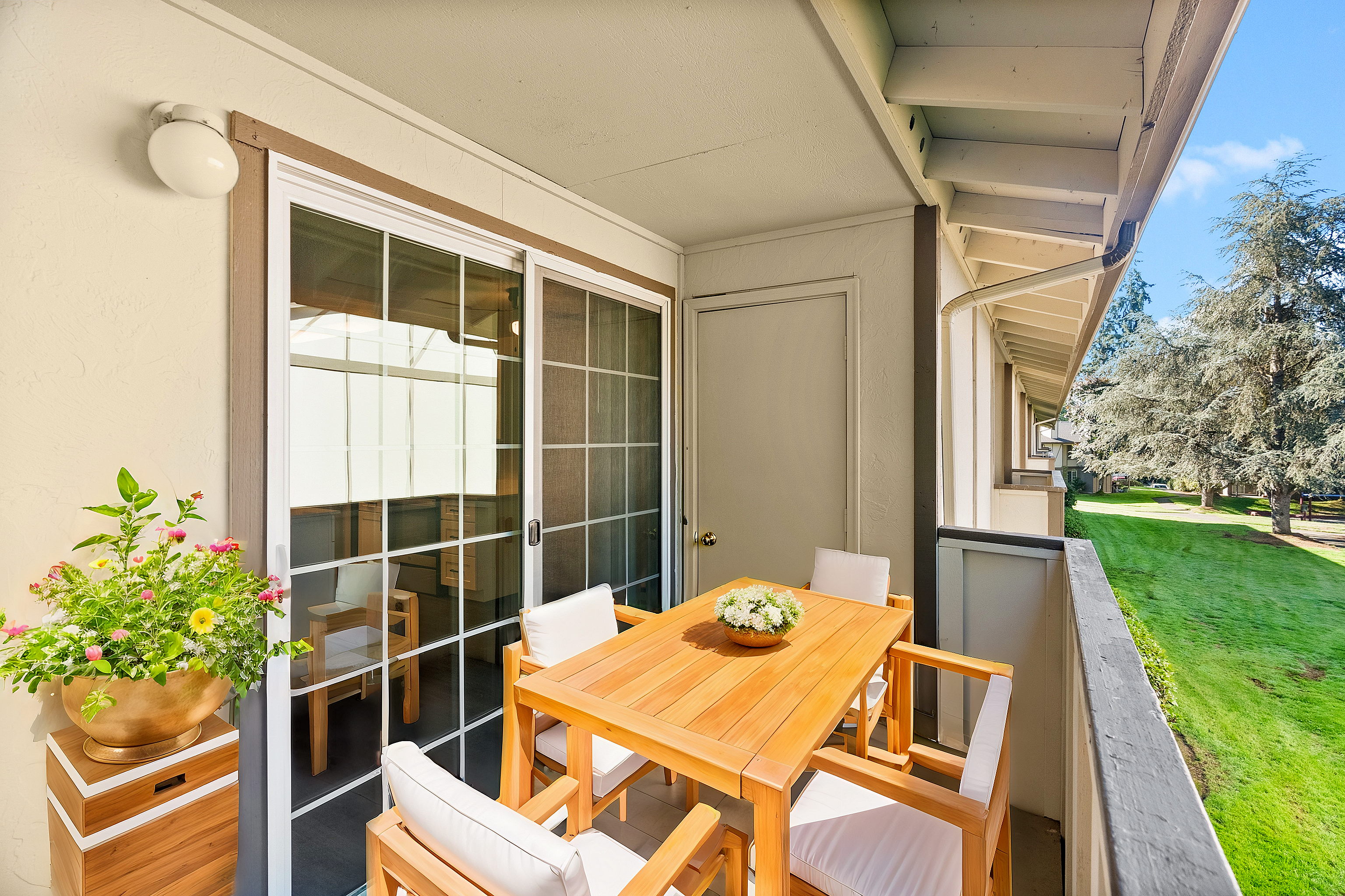 Inviting balcony with wooden table and chairs, overlooking lush greenery.