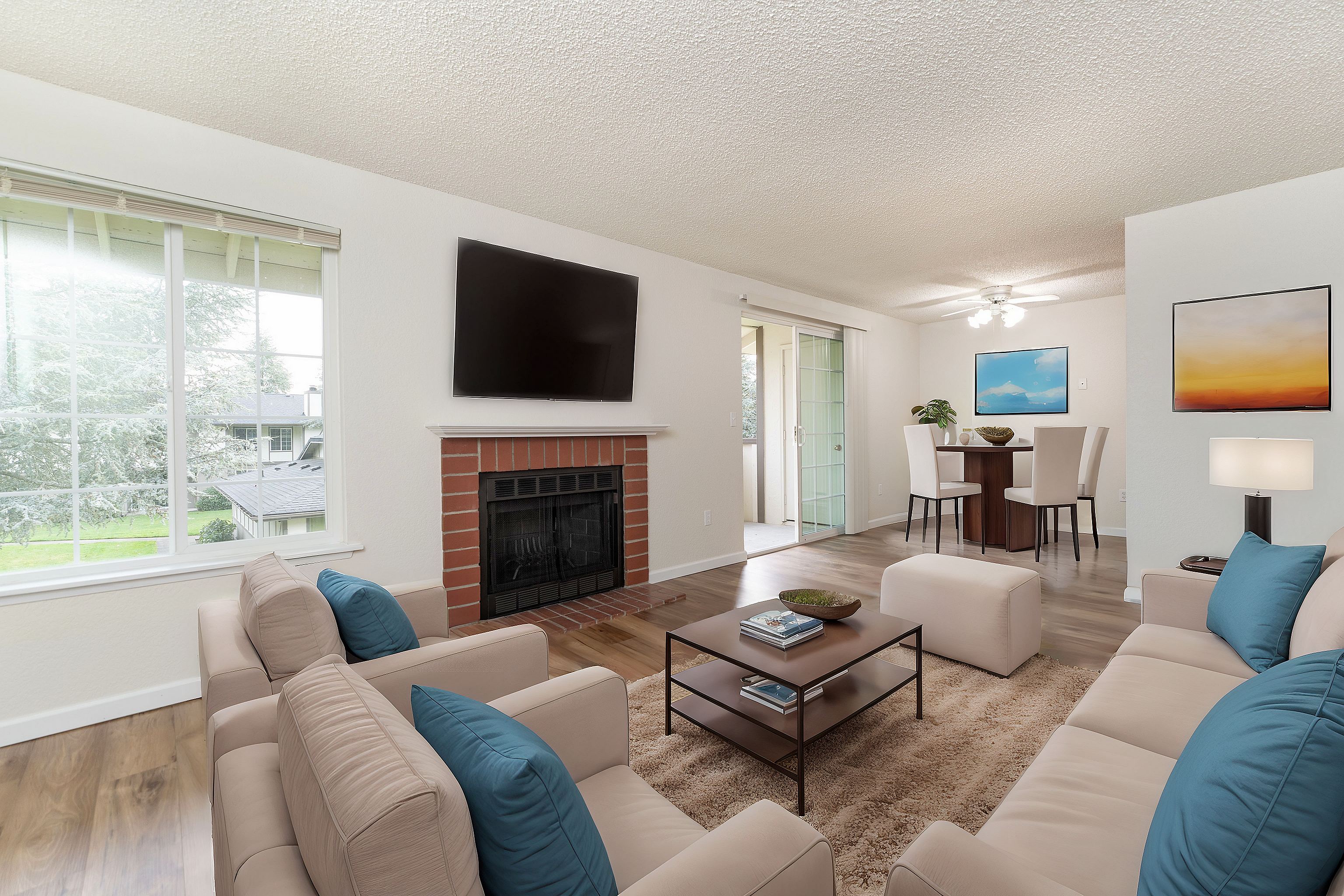 Bright, modern living room with cozy seating, a flat-screen TV above a brick fireplace, and a dining area in the background.