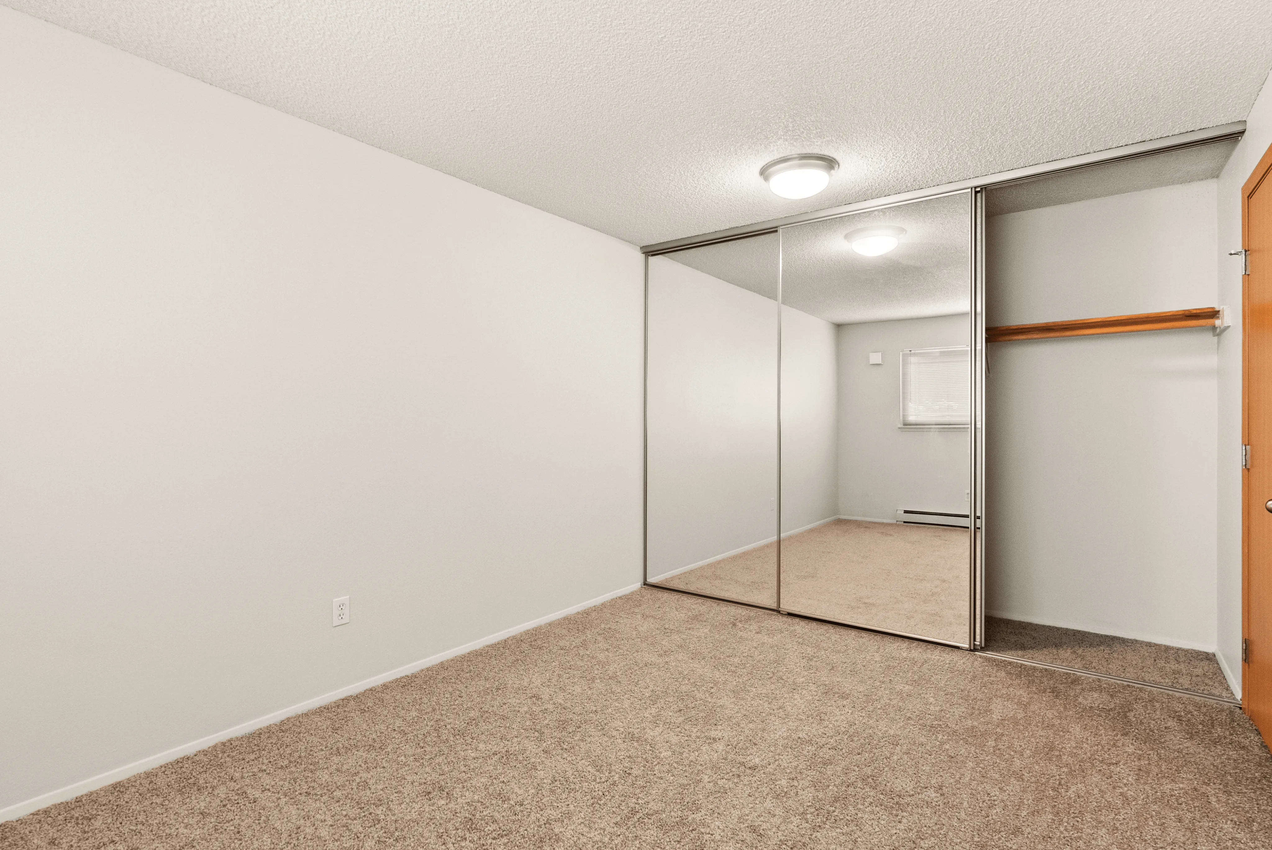 Spacious bedroom with mirrored closet doors and soft carpet flooring.