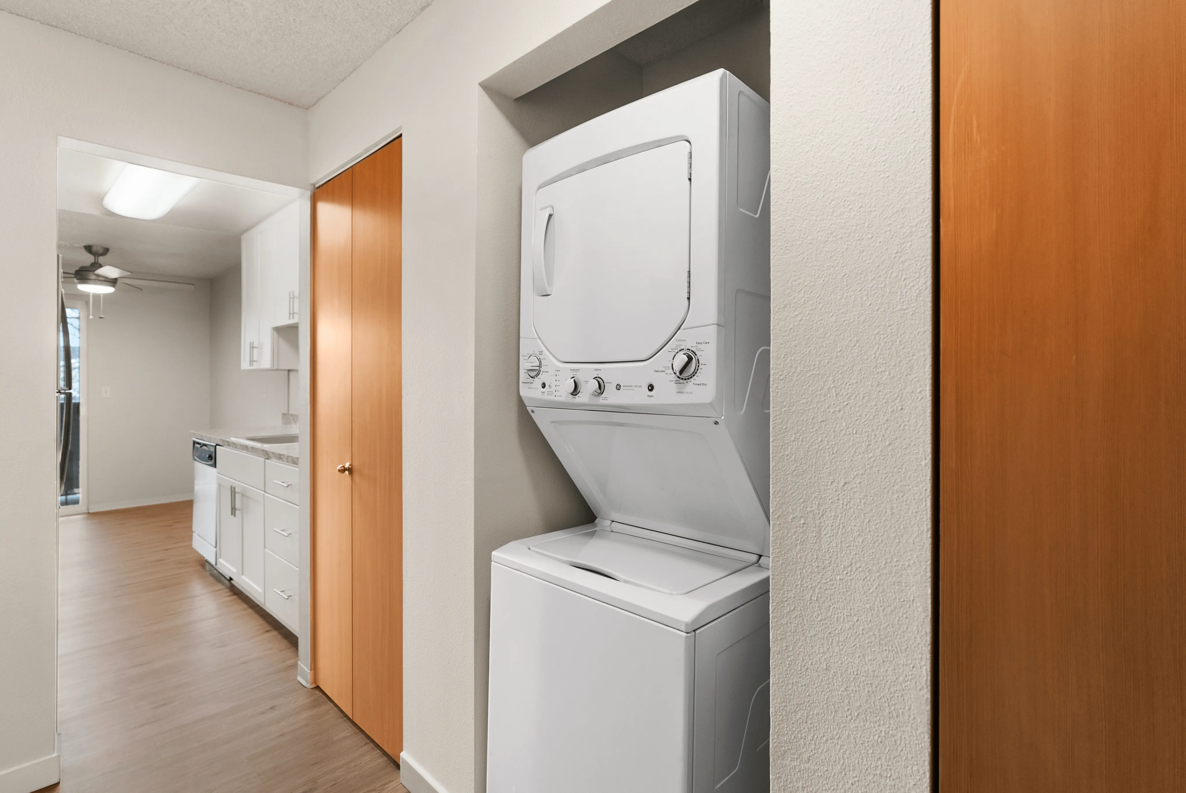 Efficient in-unit washer and dryer adjacent to a modern kitchen with white cabinetry and hardwood flooring.