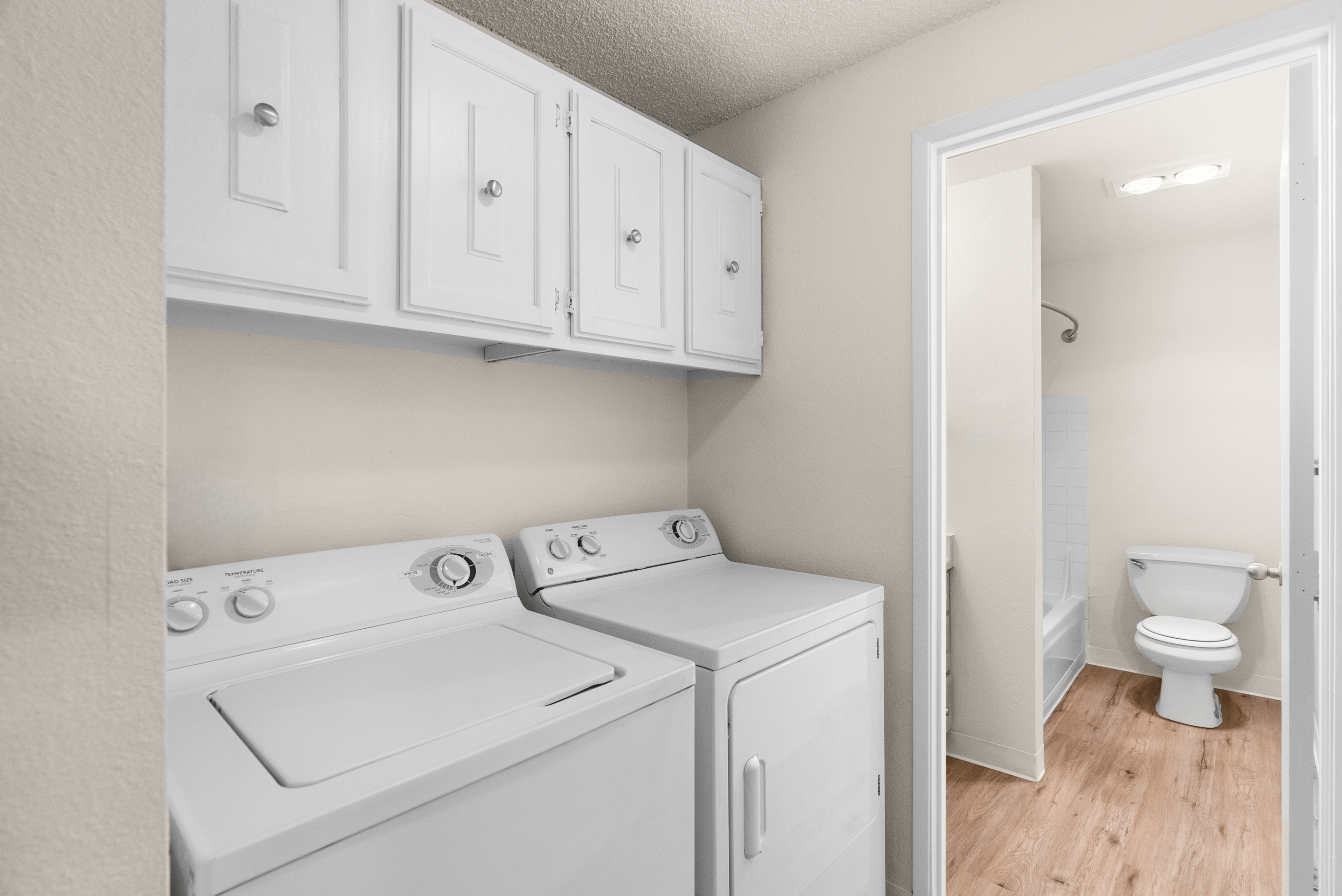 Efficient laundry area with washer, dryer, and overhead storage next to a bathroom.