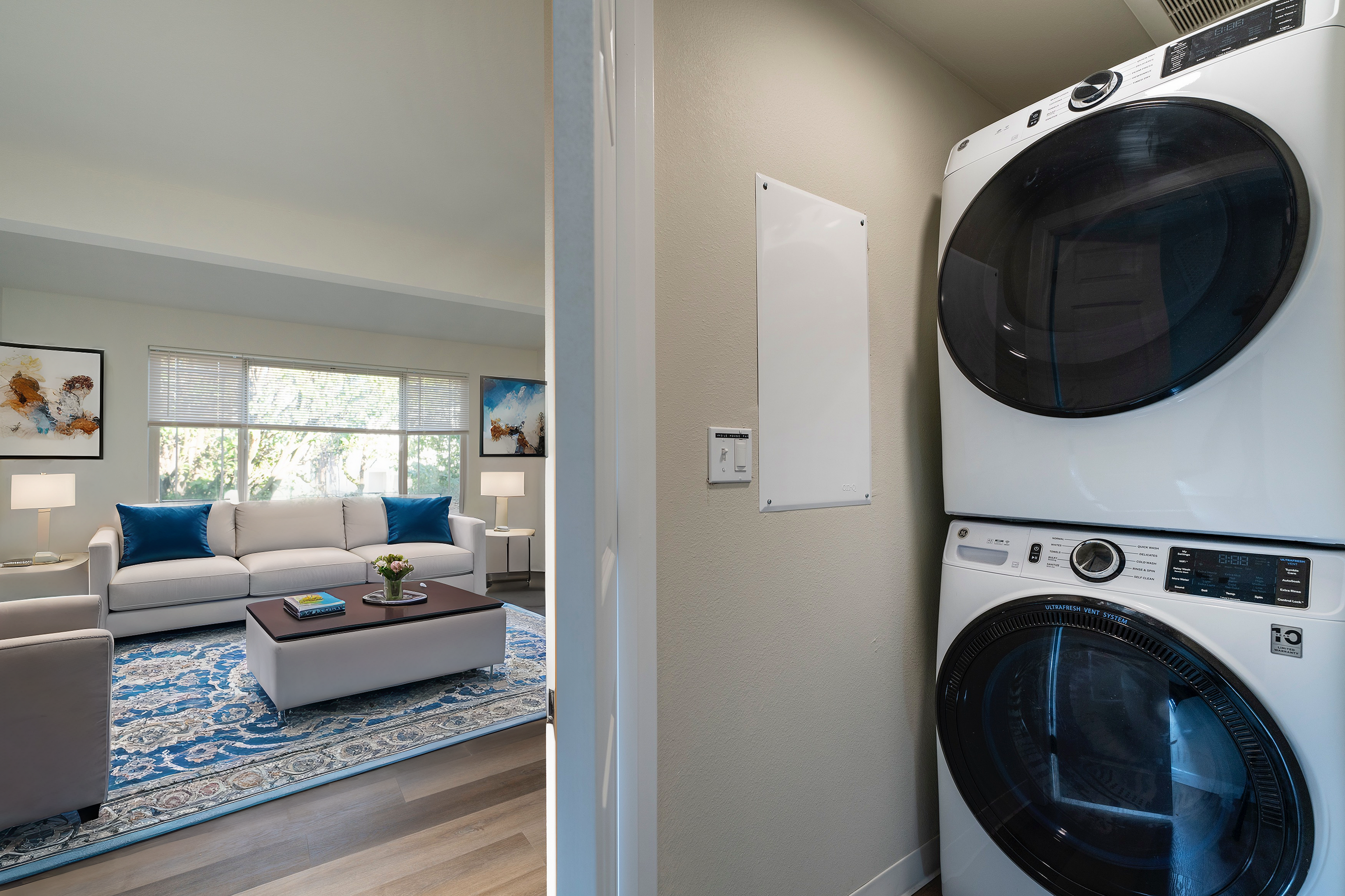 Bright living room with a stylish sofa and a stacked washer-dryer unit in a modern apartment.