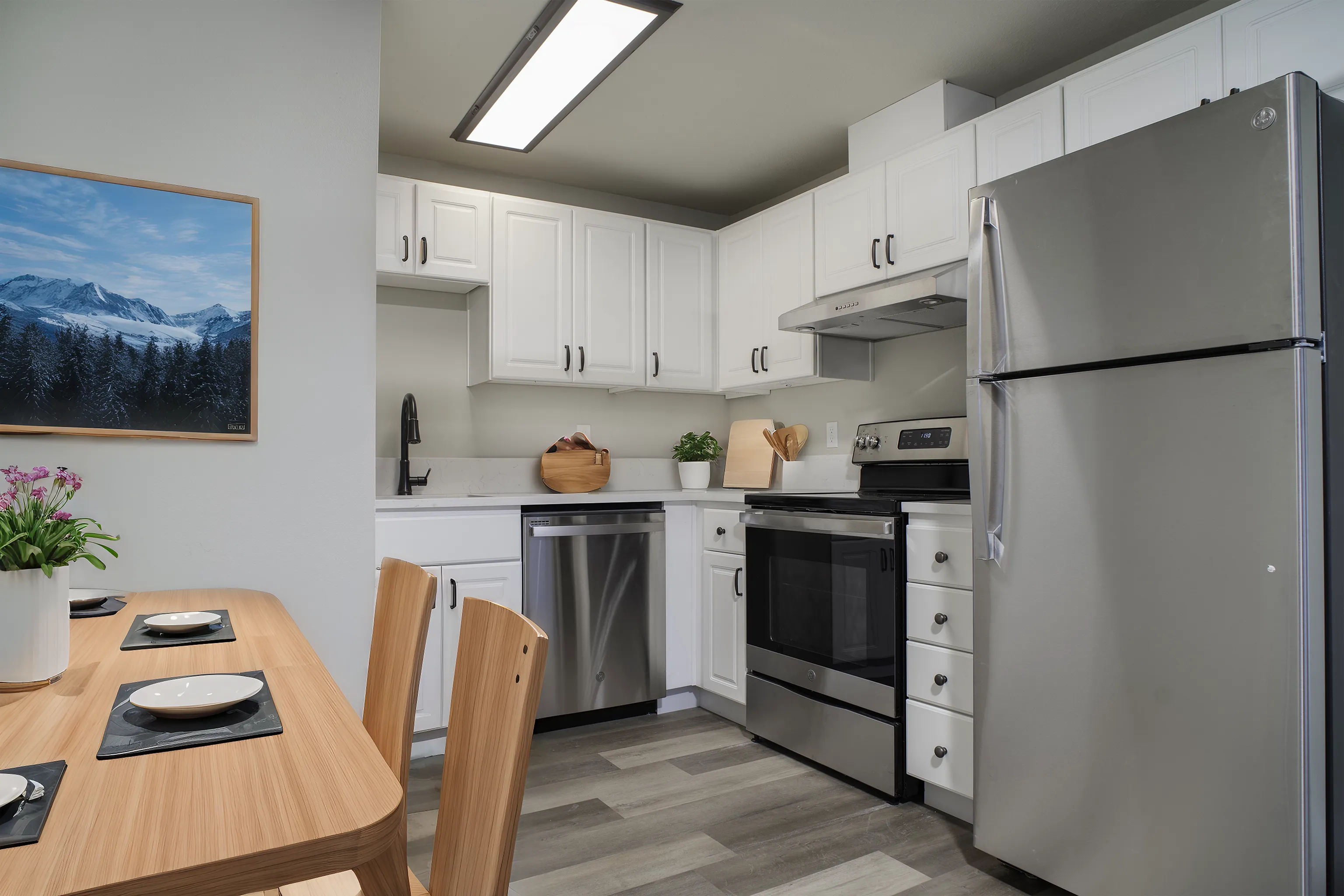 Sleek modern kitchen with stainless steel appliances, white cabinetry, and a wooden dining table set.