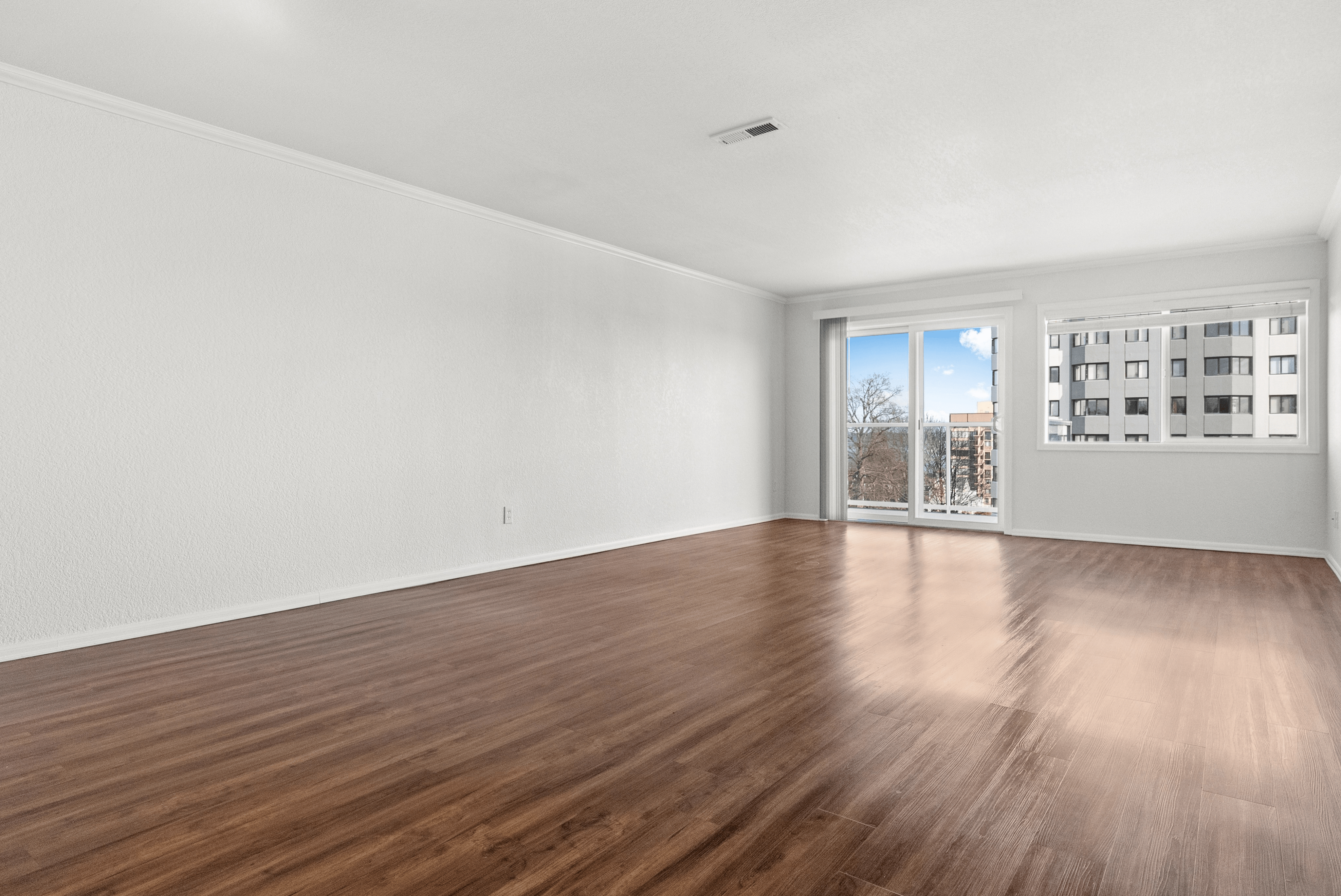 Bright and airy empty living room with large windows offering city views and wooden flooring.