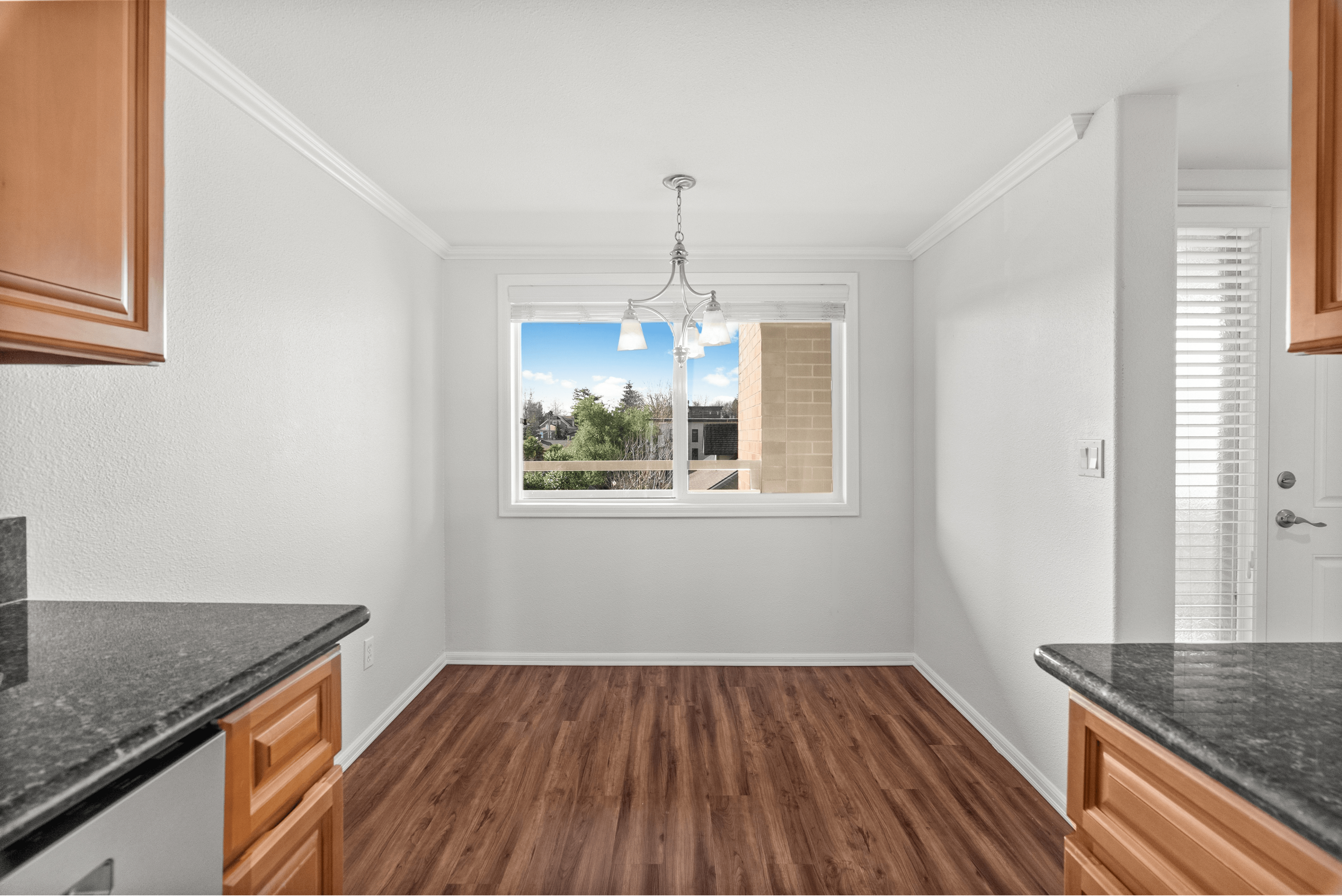 Inviting dining space featuring elegant wood floors, white walls, and a modern chandelier with a scenic window view.