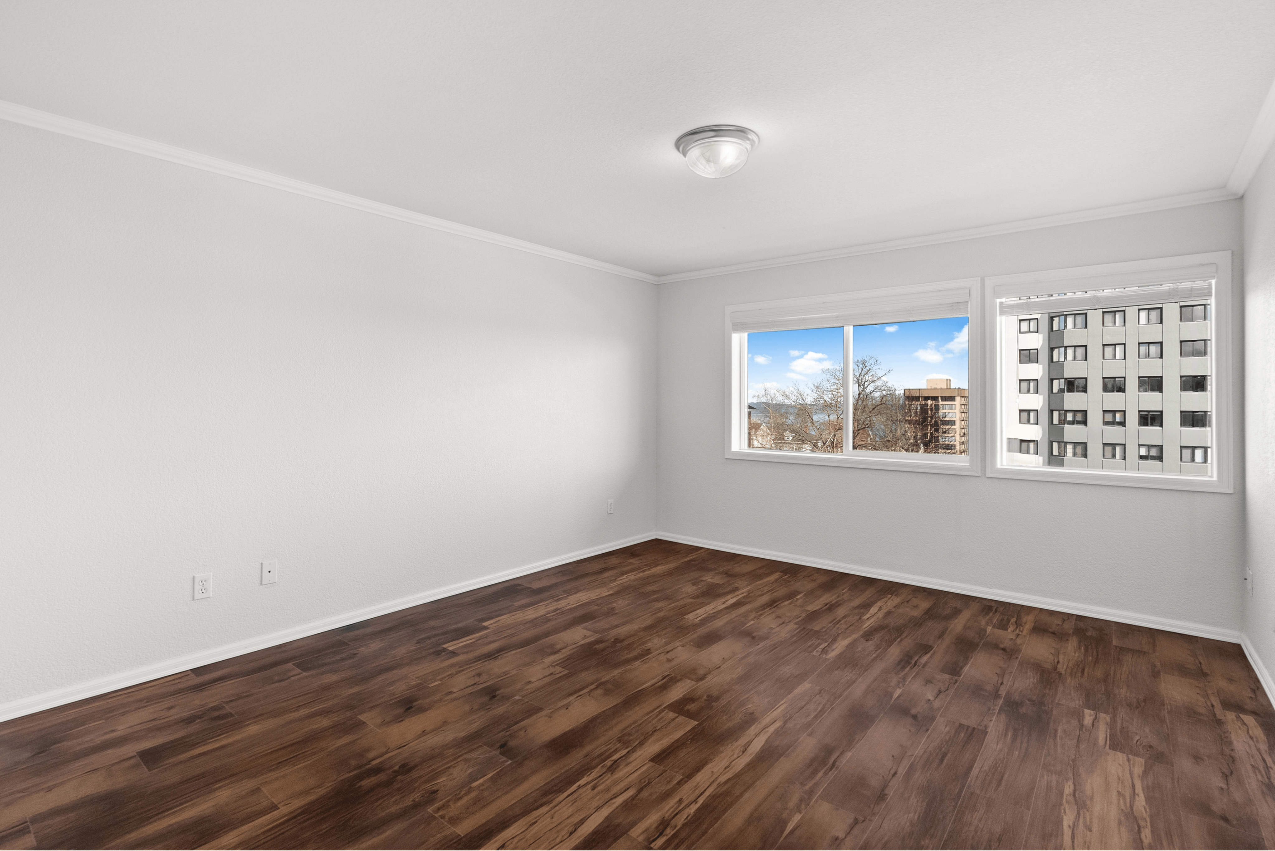 Bright empty room with large windows showcasing a city view and wooden flooring.