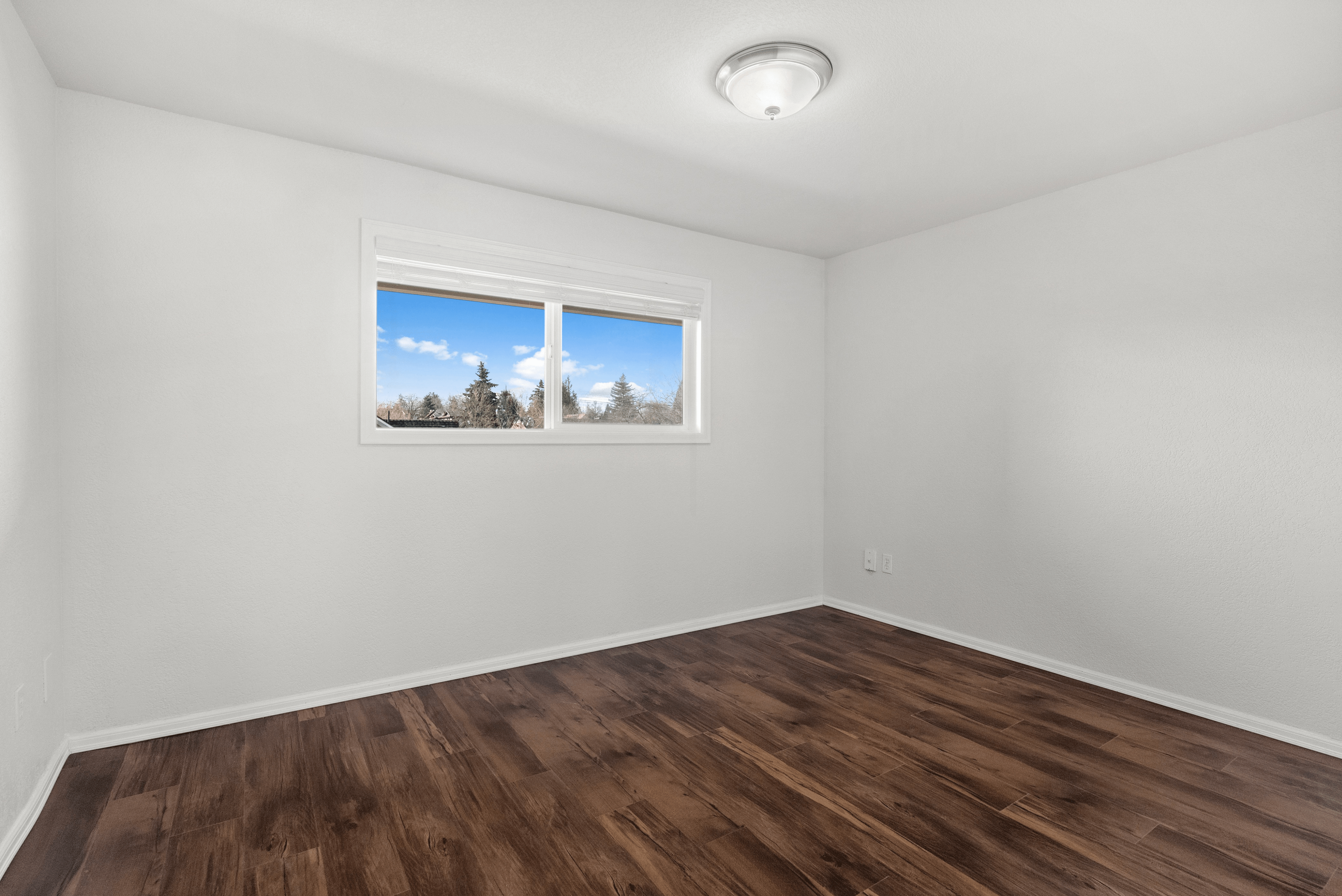 Spacious bedroom with hardwood floors and a large window offering a scenic view.