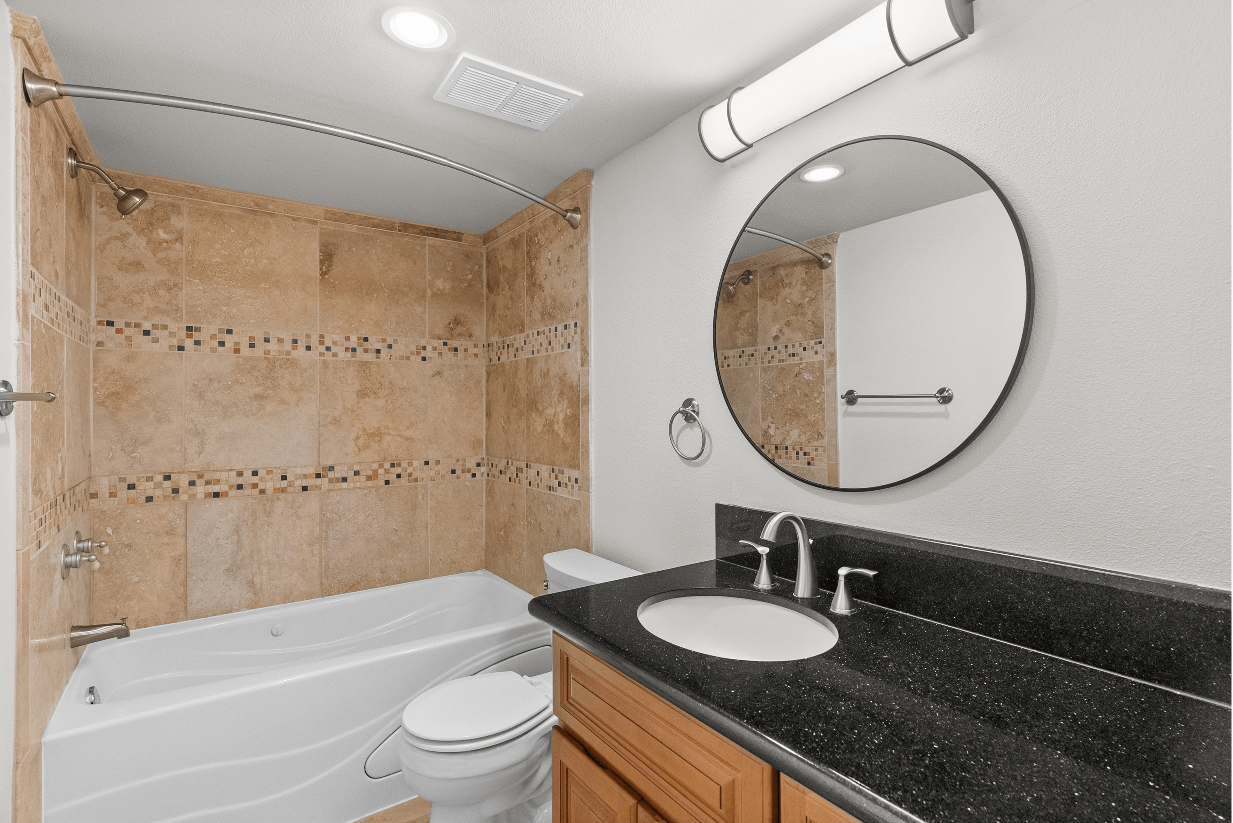Modern bathroom featuring a sleek vanity with a black countertop, circular mirror, and tiled bathtub.