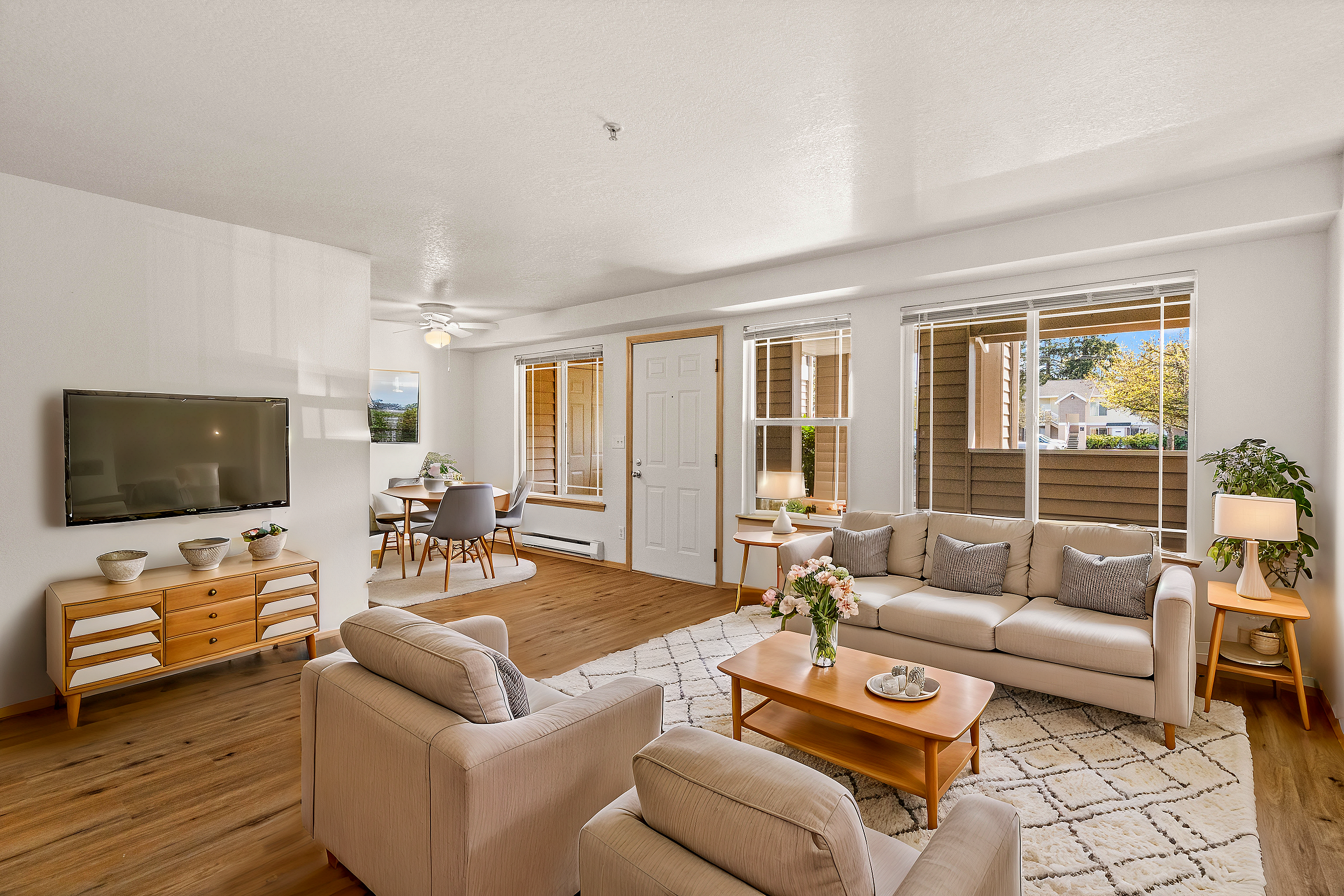 Bright and cozy living room featuring plush sofas, a dining area, and large windows with natural light.