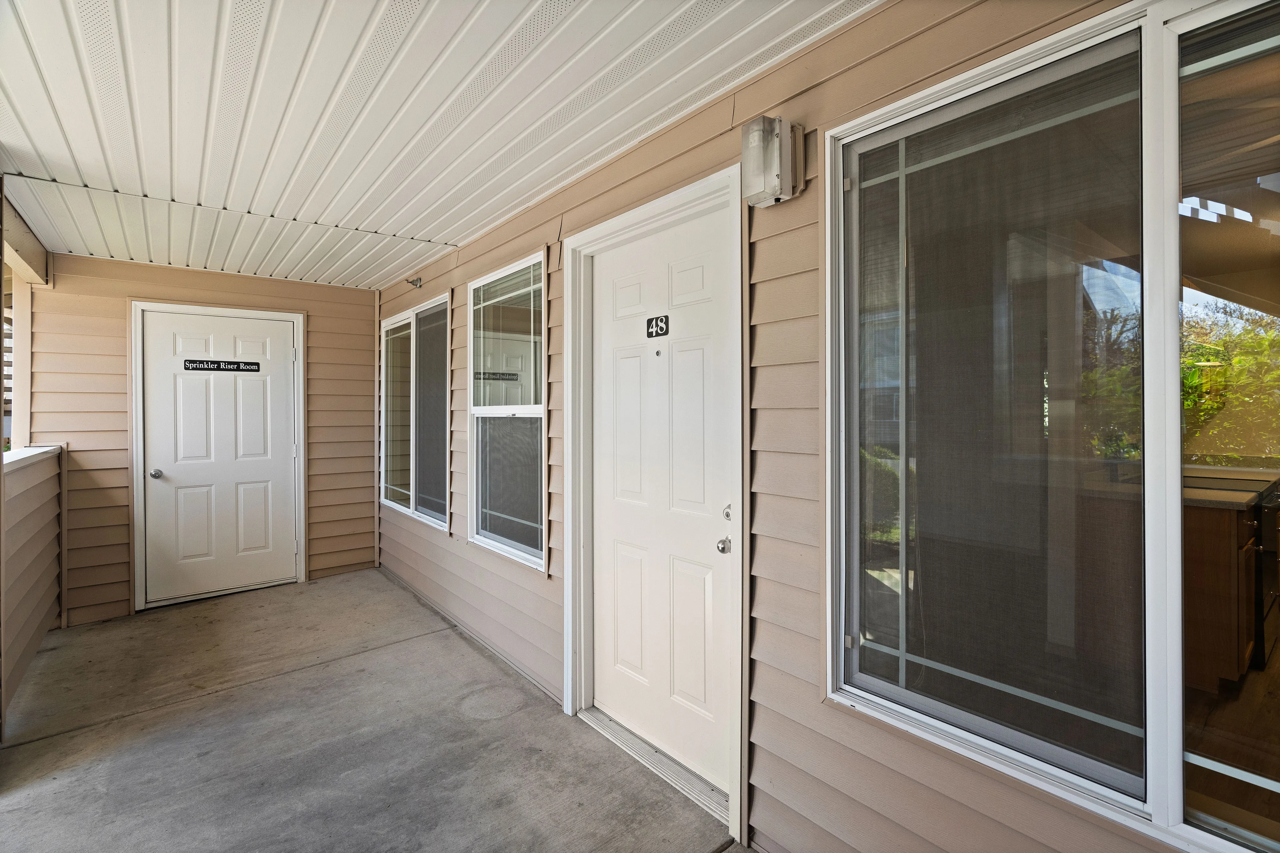 Inviting entrance to an apartment with beige siding and a white door numbered 48, featuring large windows.