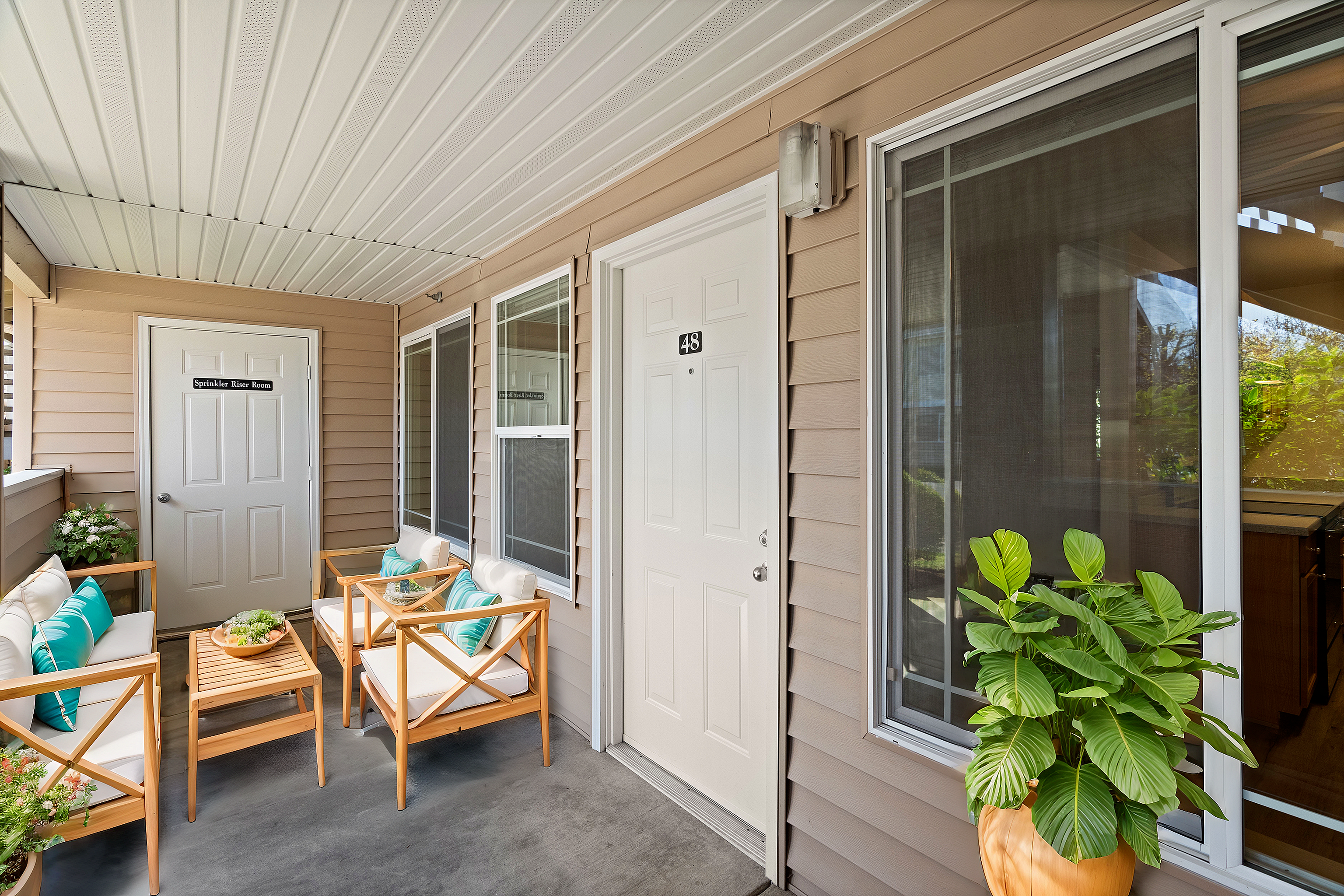 Charming outdoor patio with comfortable seating, potted plants, and a view of apartment entrance number 48.
