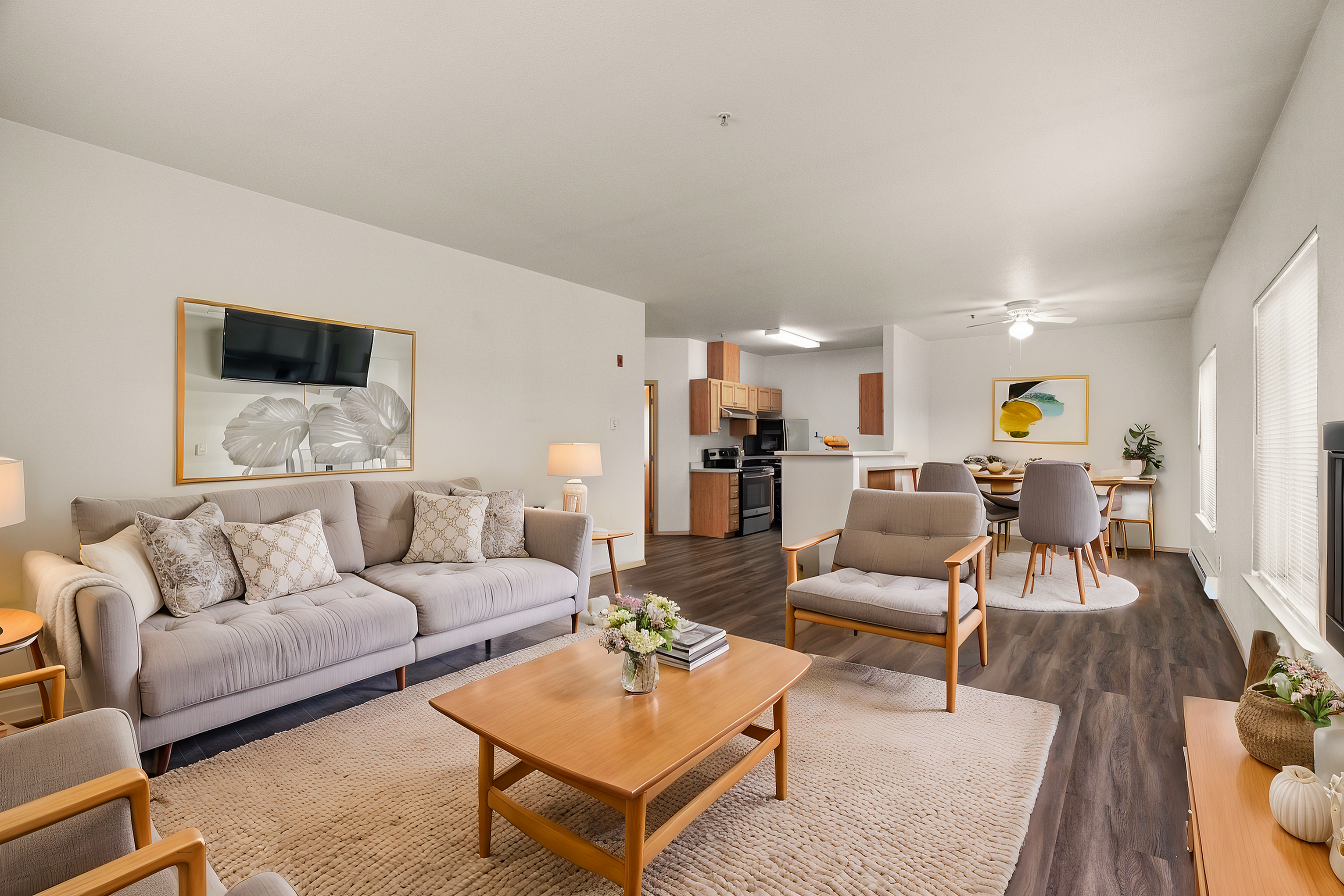 Bright and inviting living room with modern decor, featuring a comfortable gray sofa, stylish armchairs, a sleek coffee table, and a view into the open kitchen and dining area.