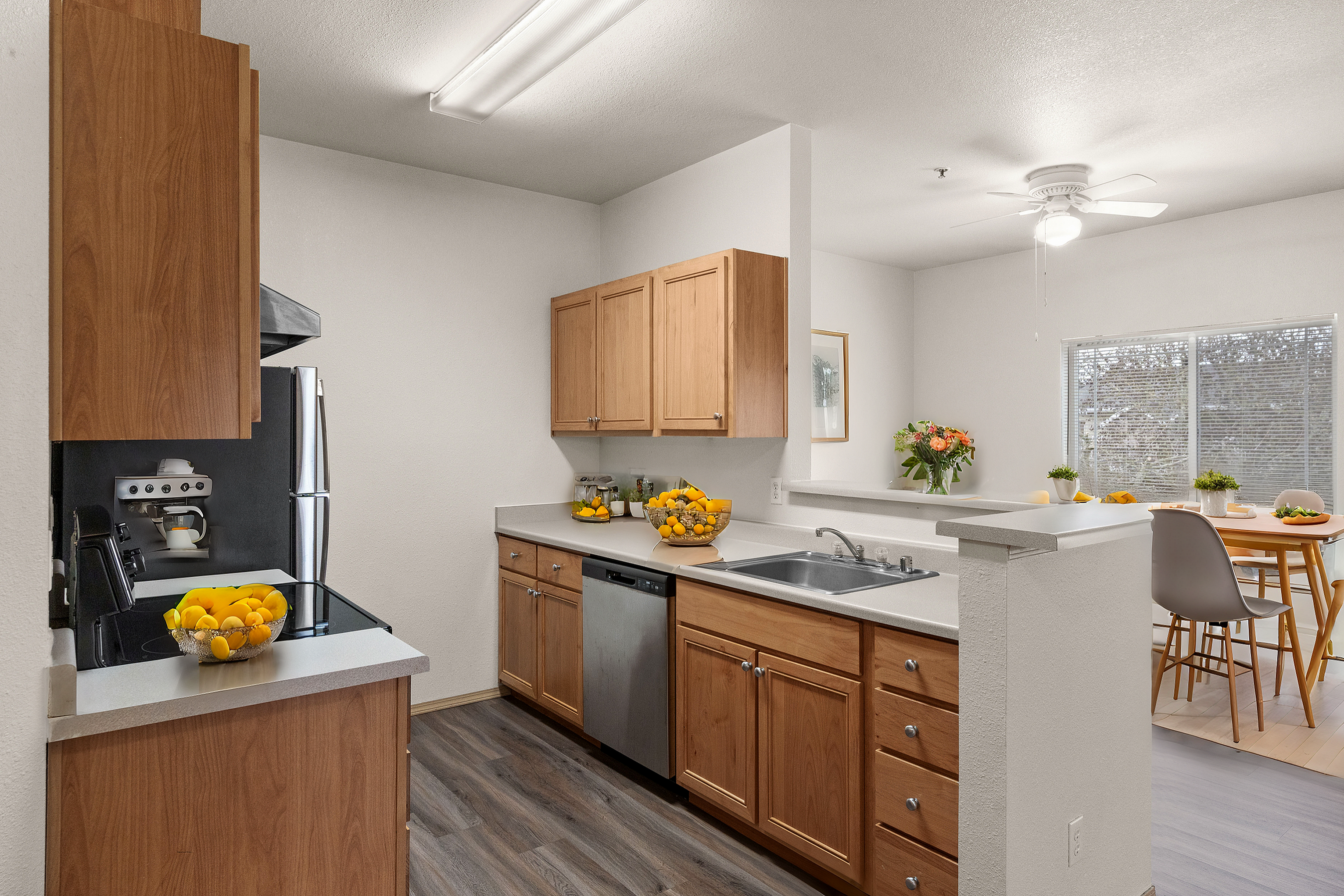 Modern kitchen with wooden cabinetry, sleek countertops, and stainless steel appliances; adjacent open dining area with large windows and stylish decor.