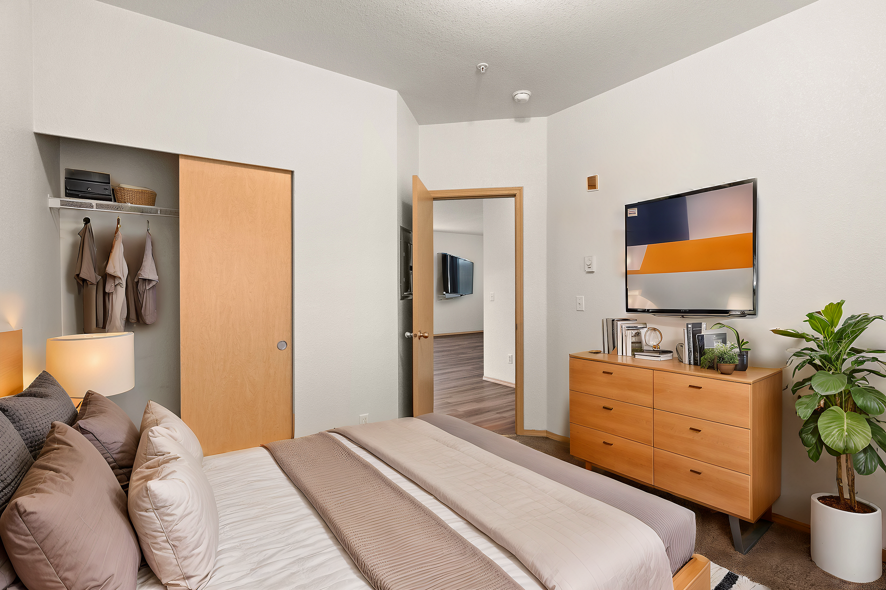 Elegant bedroom with cozy bedding, sophisticated decor, and wall-mounted TV, enhanced by natural lighting and a chic wooden dresser.