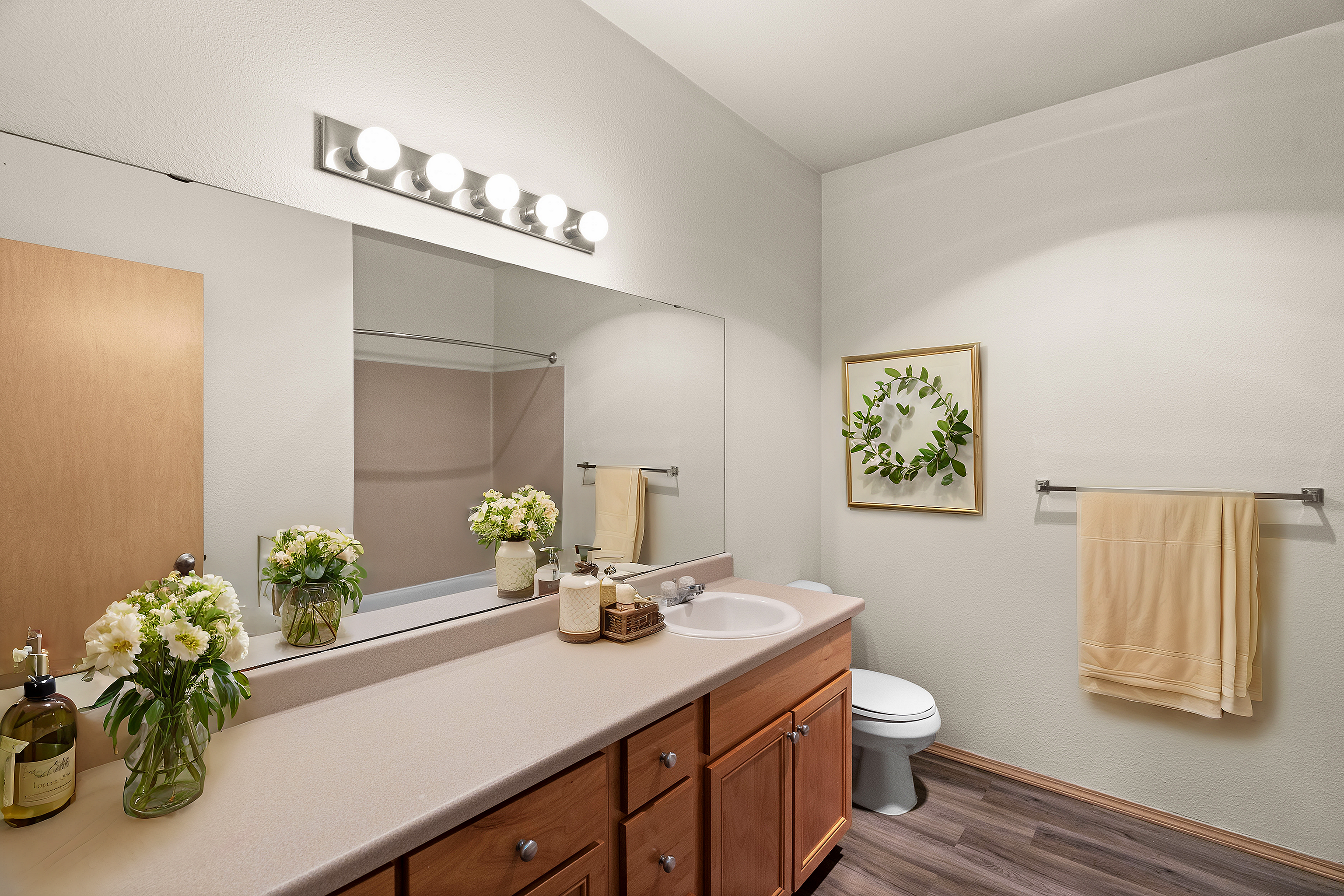 Bright and inviting bathroom with elegant wooden cabinetry, stylish floral decor, and modern lighting.