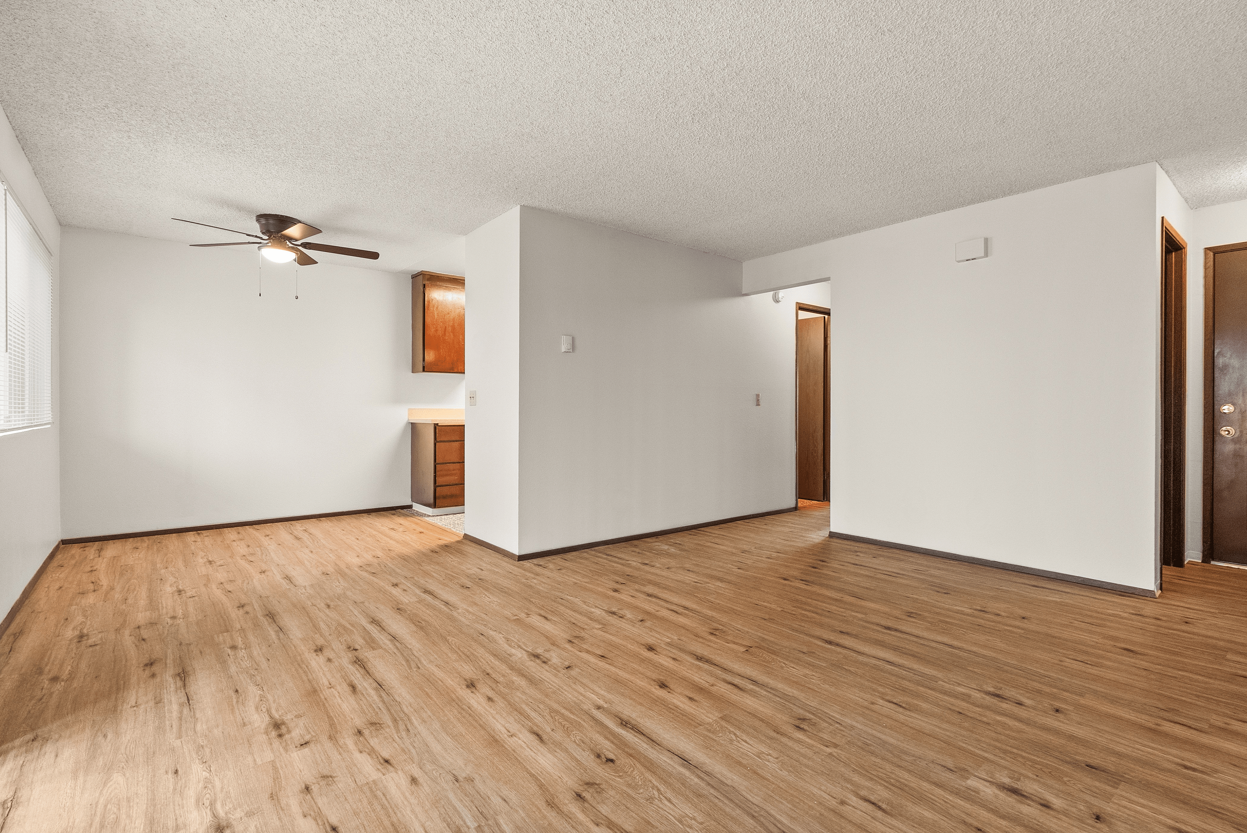Inviting open-concept apartment with cozy hardwood floors and abundant natural light, featuring a stylish ceiling fan.