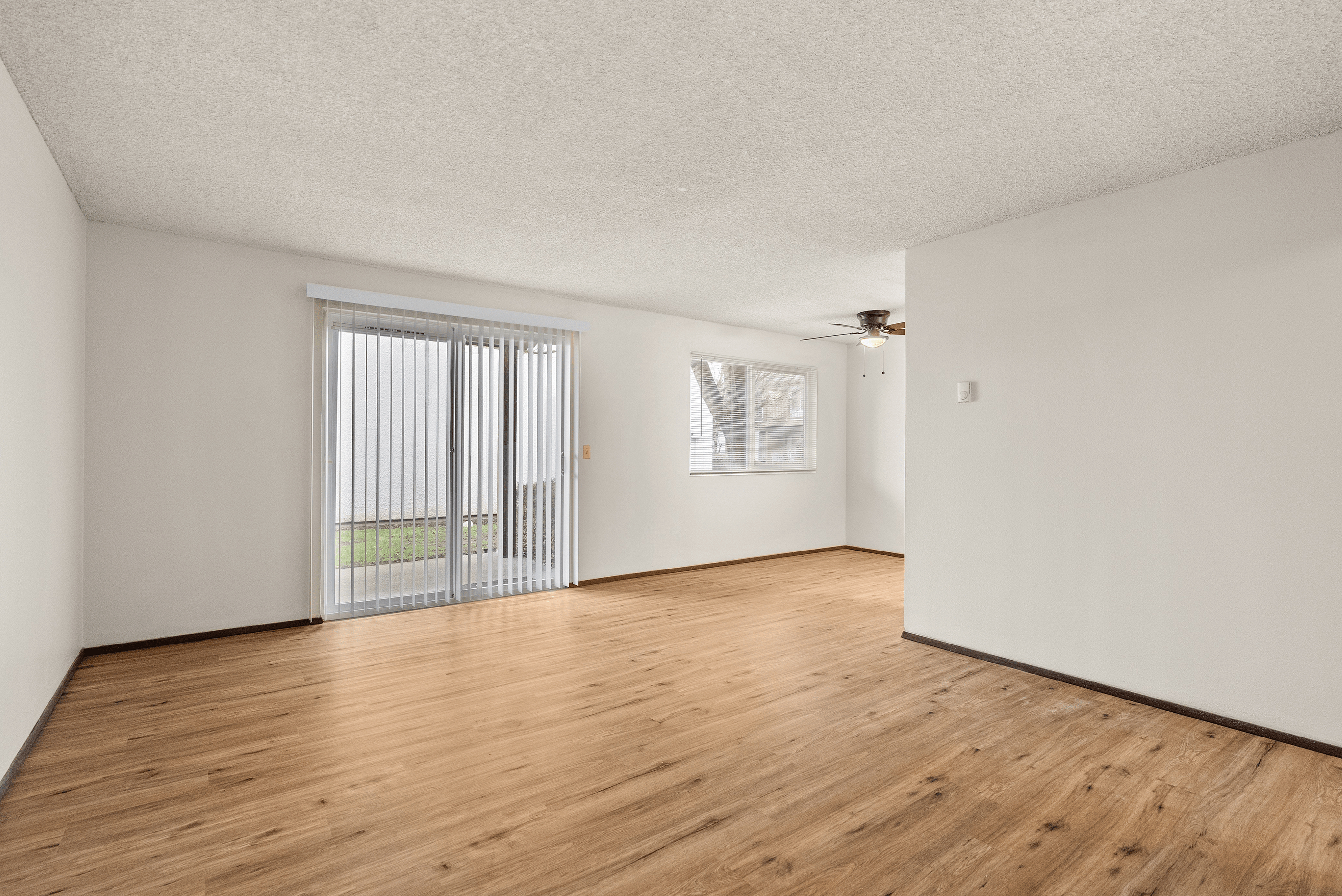 Bright and spacious living area featuring elegant wood flooring, large windows, and sliding glass doors leading to a charming outdoor space.