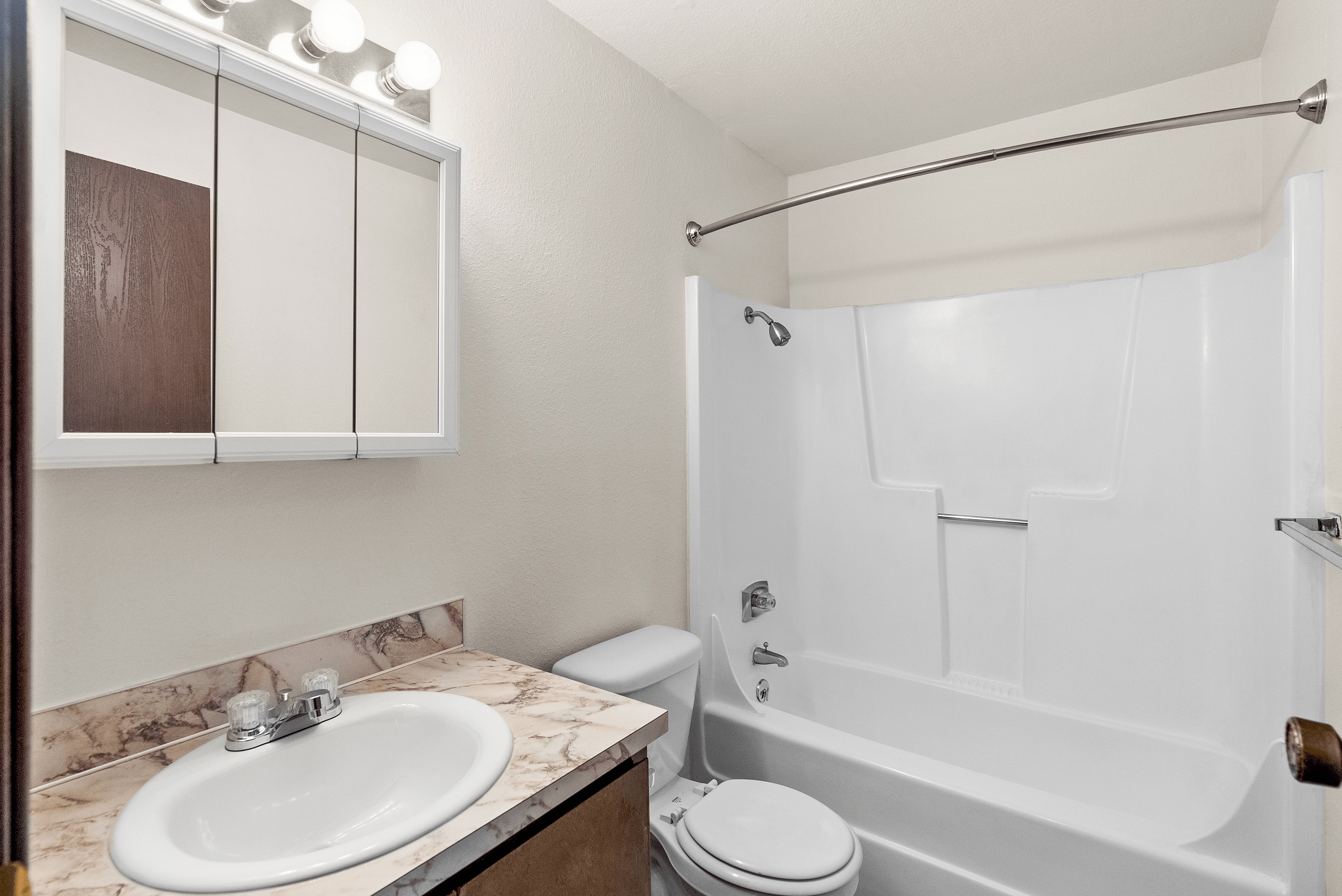 Pristine bathroom featuring a sleek marble countertop, elegant mirror cabinet, and modern bathtub with a curved shower rod.