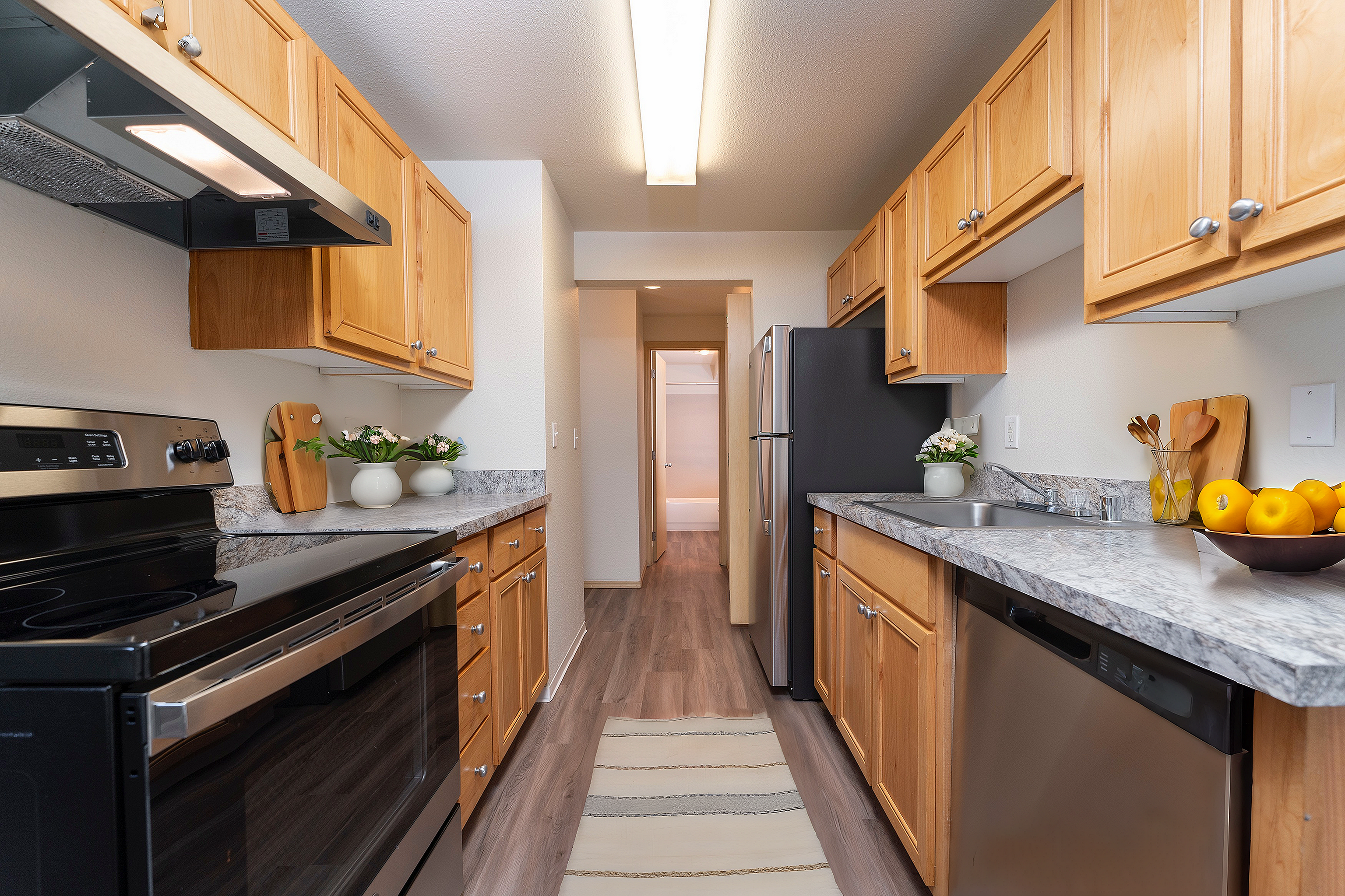 Modern galley kitchen with sleek stainless steel appliances, warm wooden cabinets, and elegant granite countertops.