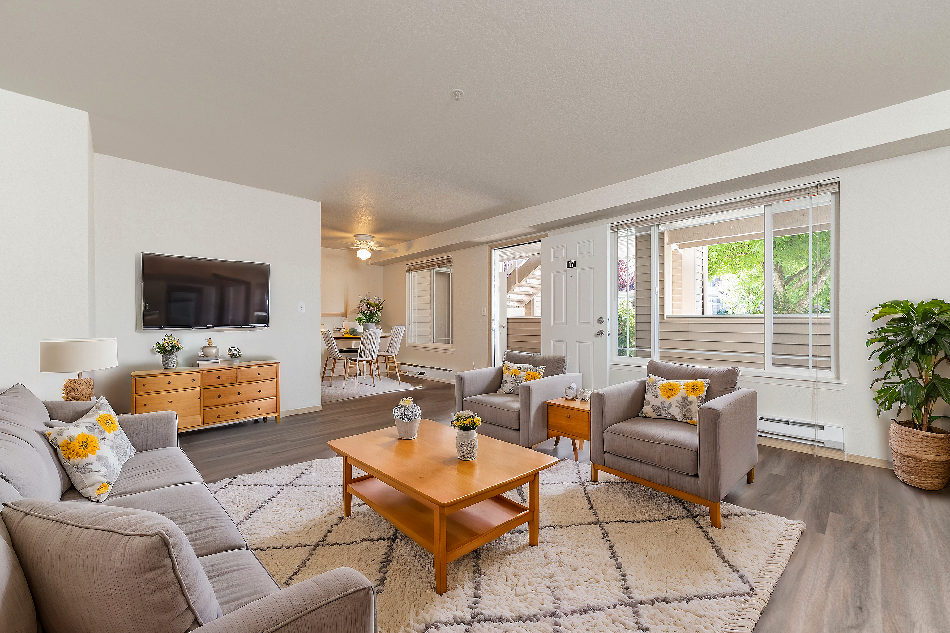 Bright and inviting living room with modern furnishings, large windows providing natural light, and an elegant dining area in the background.