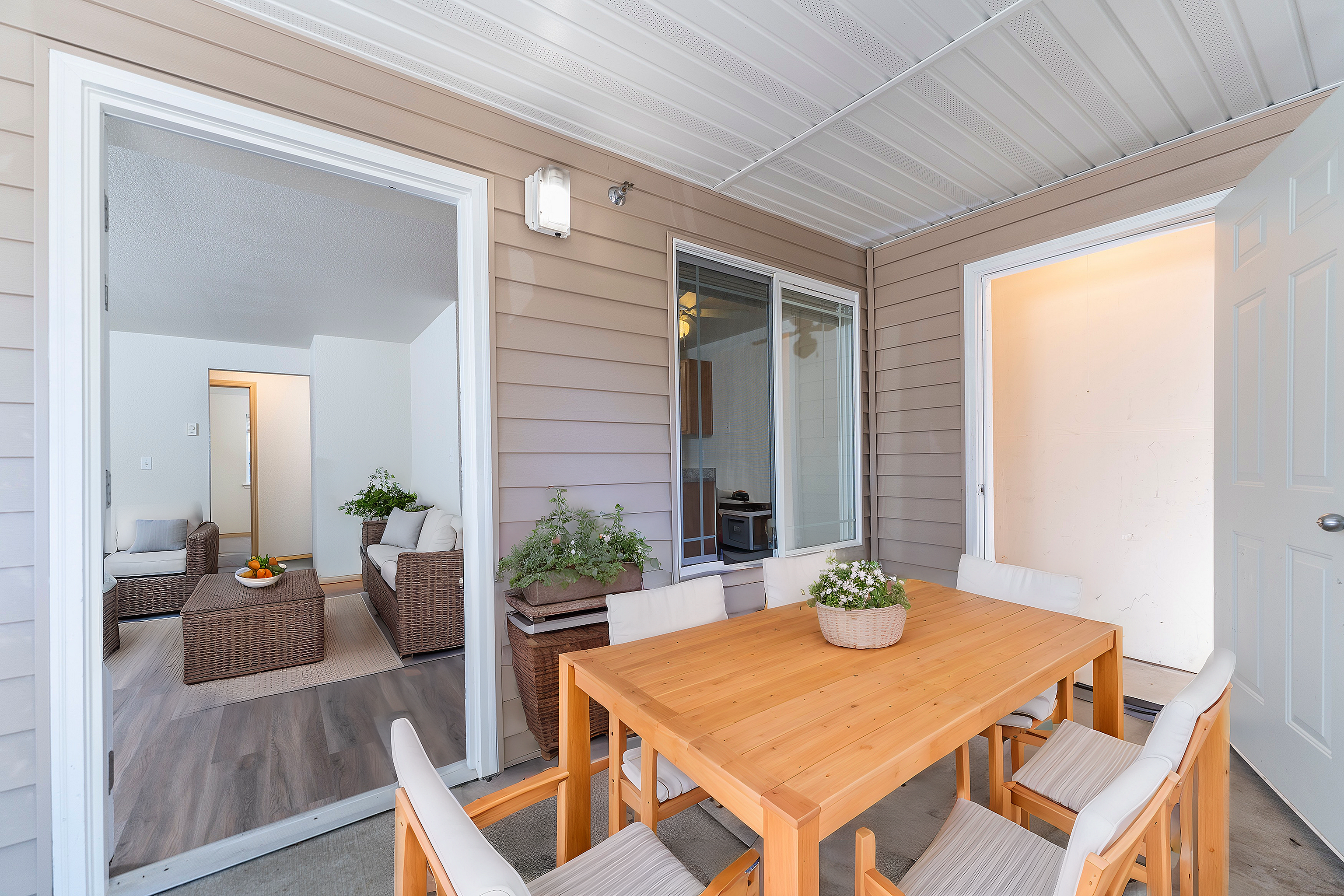 Charming covered patio leading to a cozy living room with wicker furniture, offering a perfect blend of indoor-outdoor living.