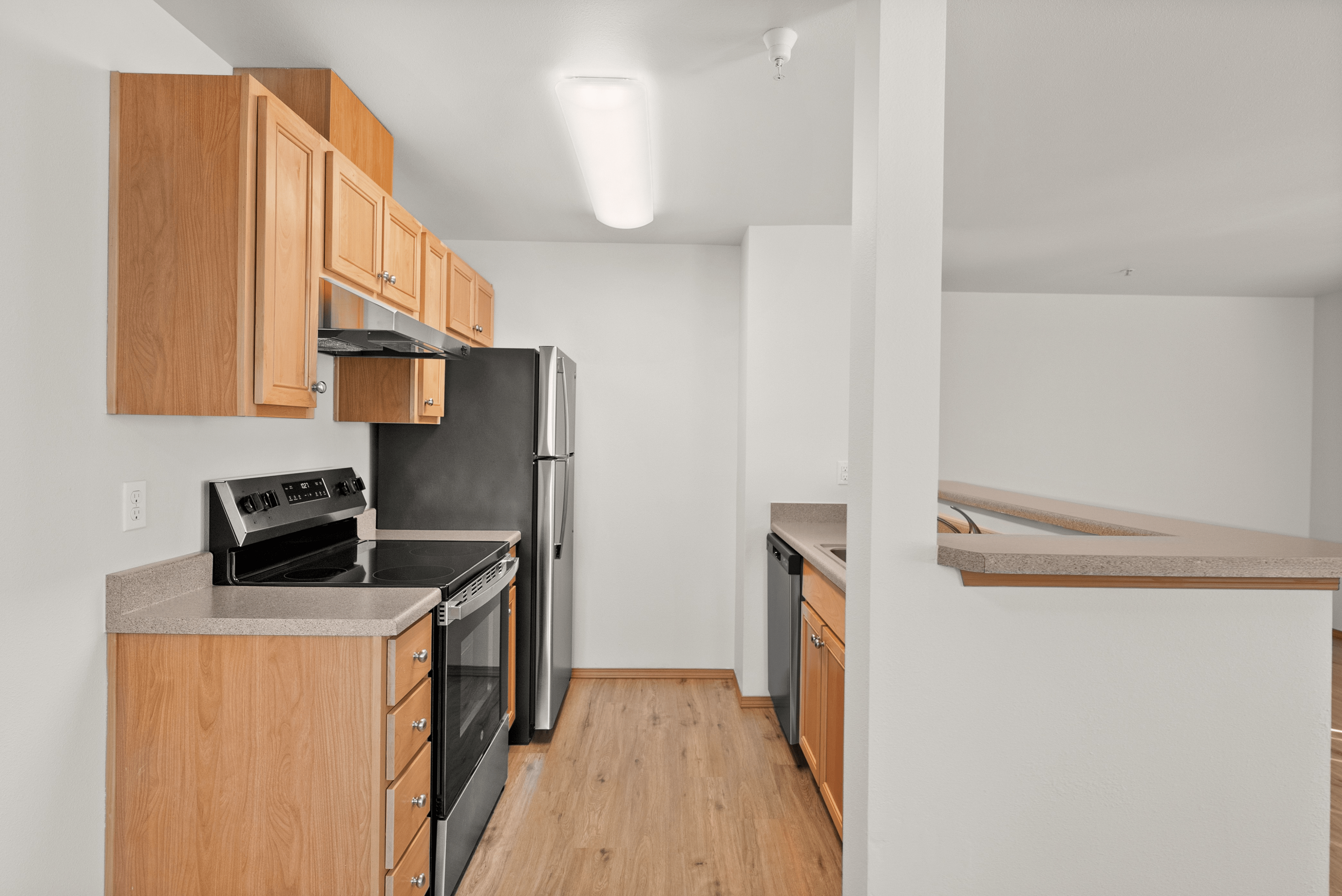 Modern kitchen with stainless steel appliances, light wooden cabinets, and laminate flooring, perfect for culinary enthusiasts.