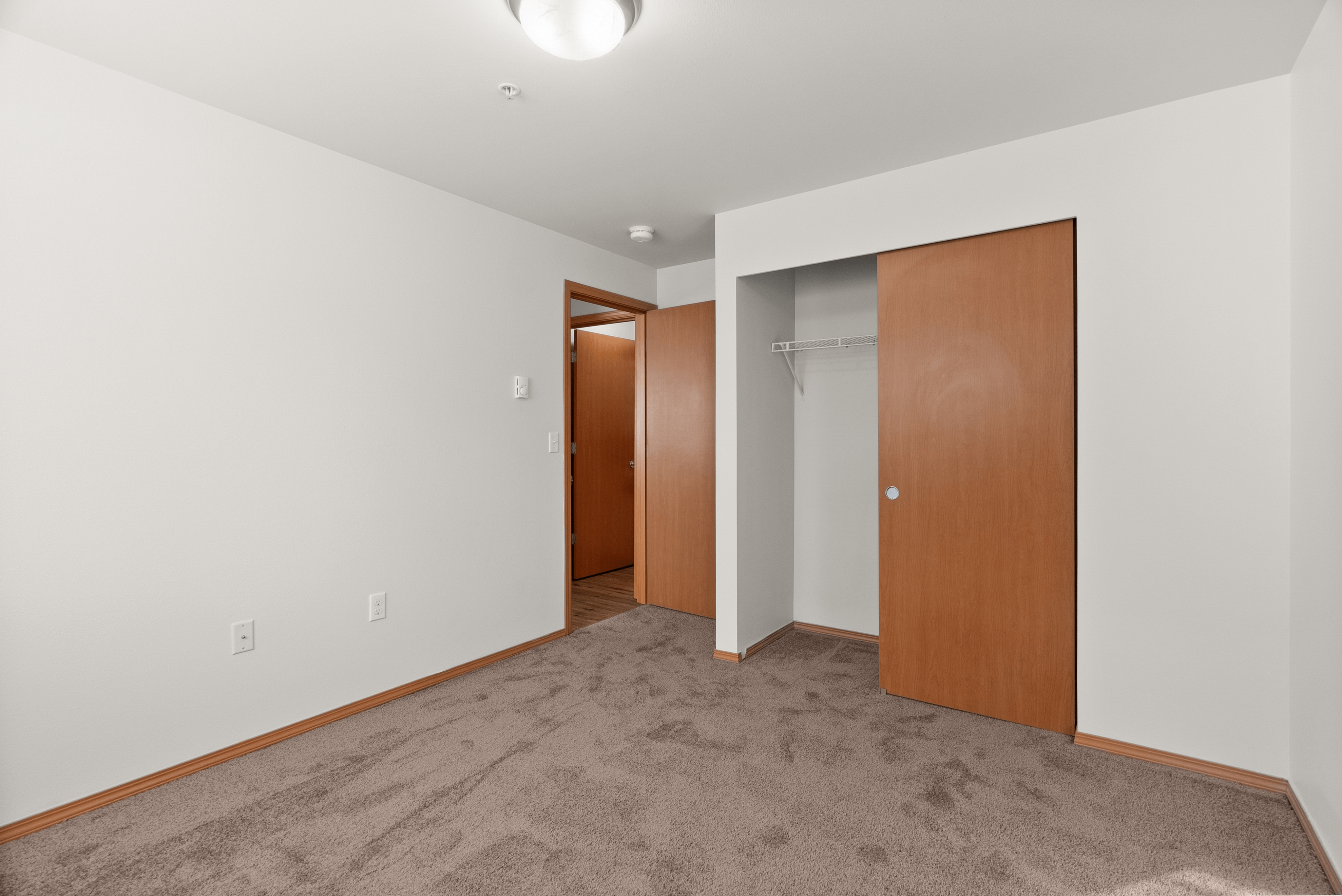 Inviting bedroom with plush carpet, ample closet space, and sleek wooden doors for a cozy living experience.
