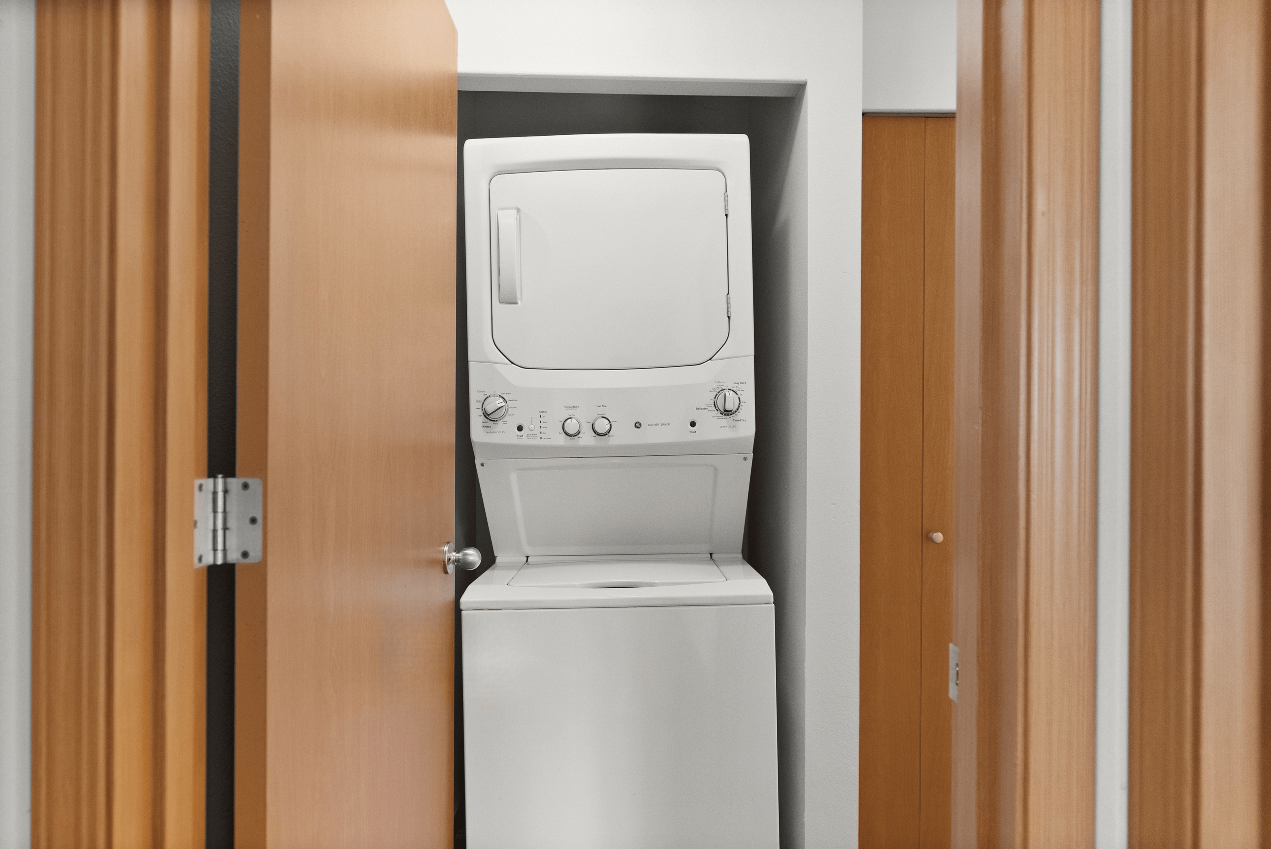Compact laundry area with a modern stackable washer and dryer set, neatly integrated into a closet space with wooden doors.