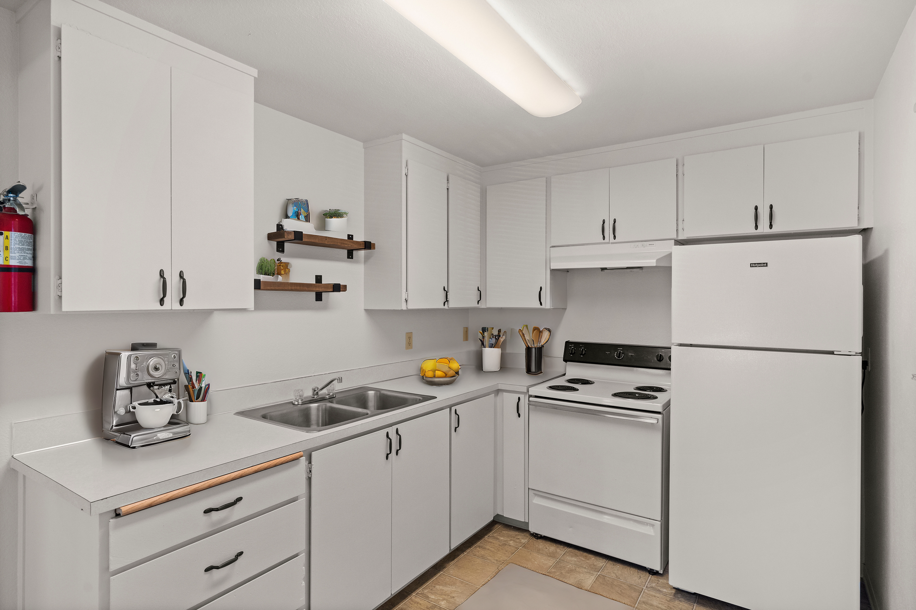 Bright and modern kitchen with white cabinetry, sleek countertops, and elegant open shelving, featuring a stylish coffee machine and essential appliances.