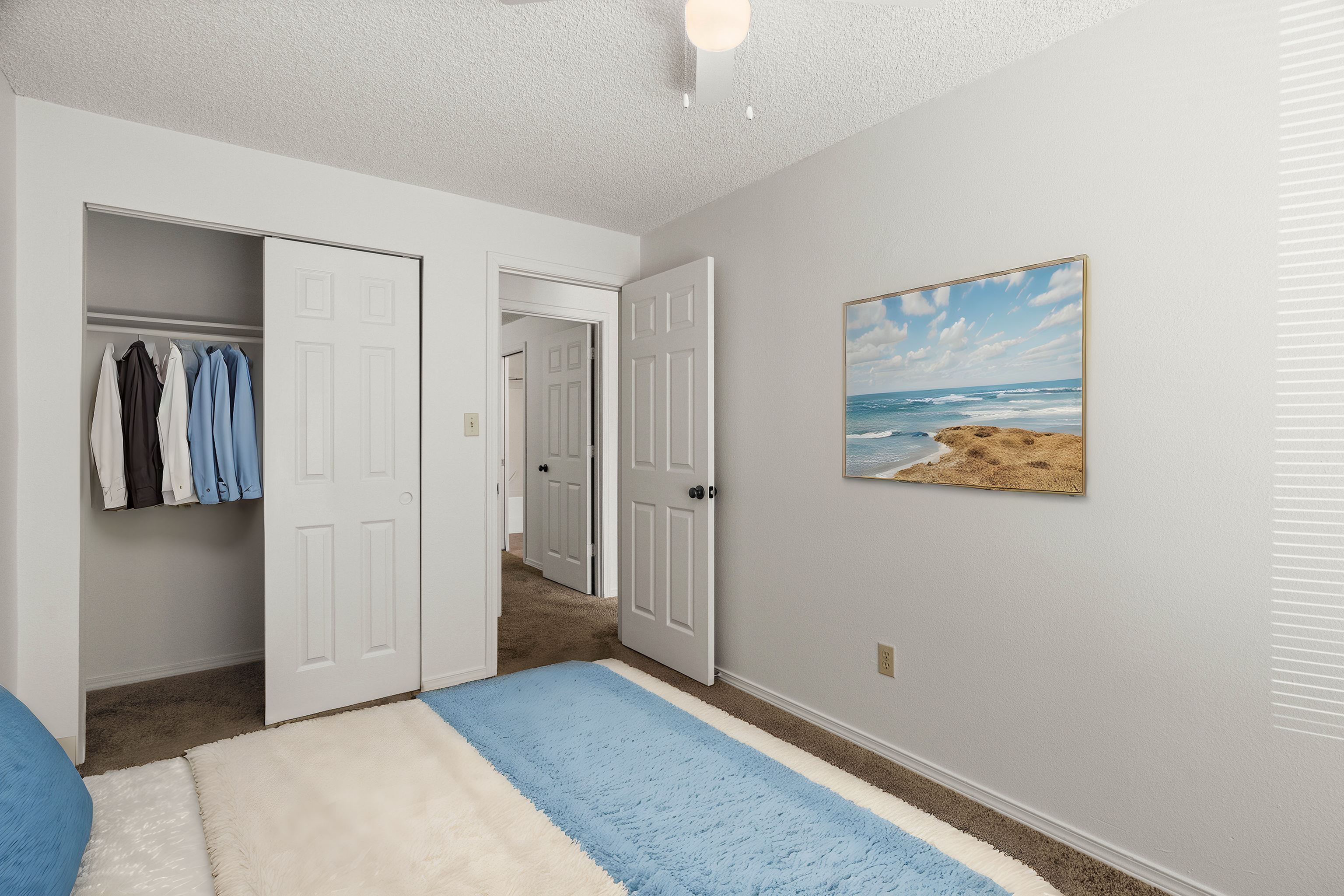 Bright bedroom with cozy blue and white bedding, spacious closet with organized shirts, and serene coastal artwork on the wall.