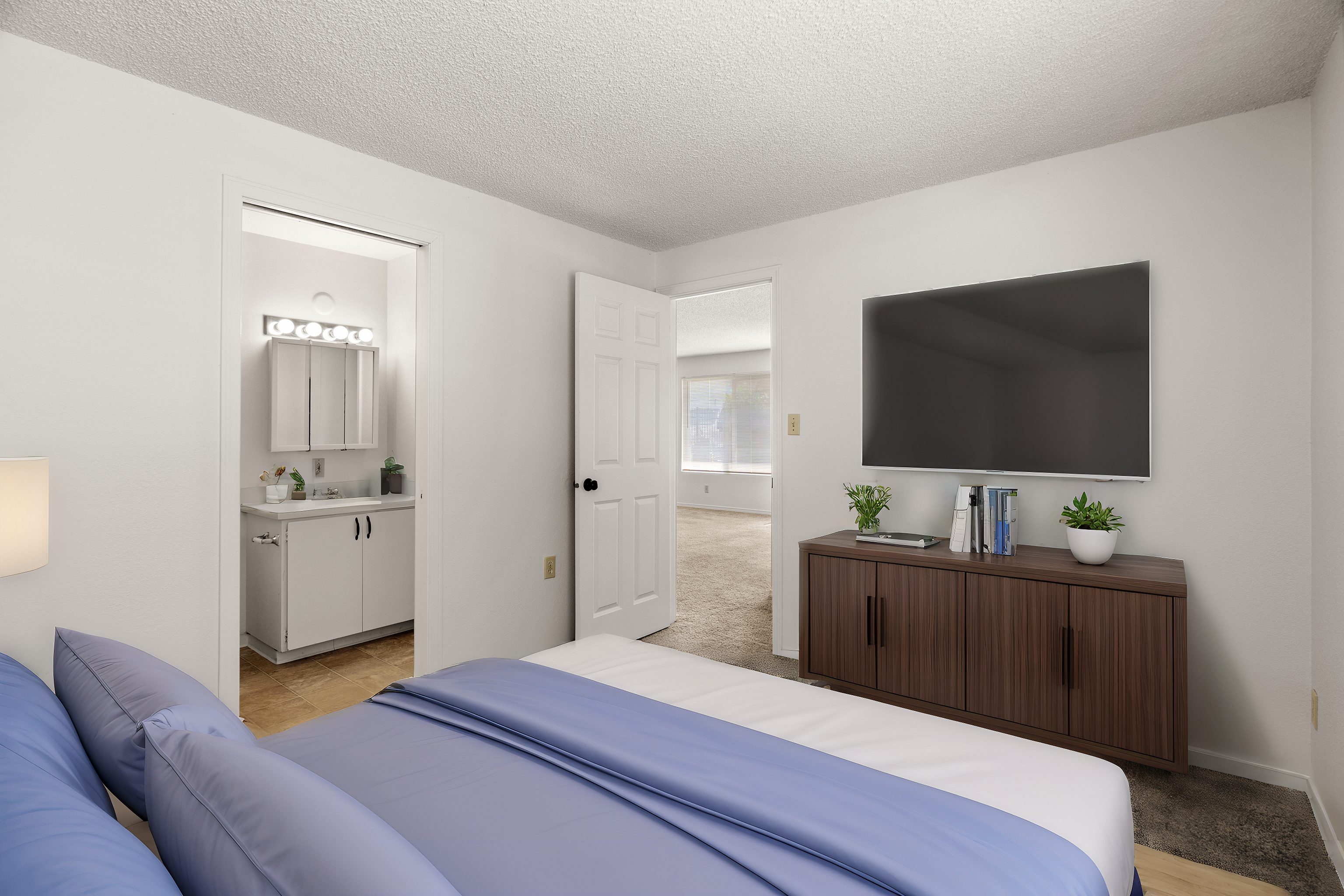 Cozy bedroom with a sleek TV and dresser, leading to a bright bathroom. Spacious and inviting design with plush bedding.
